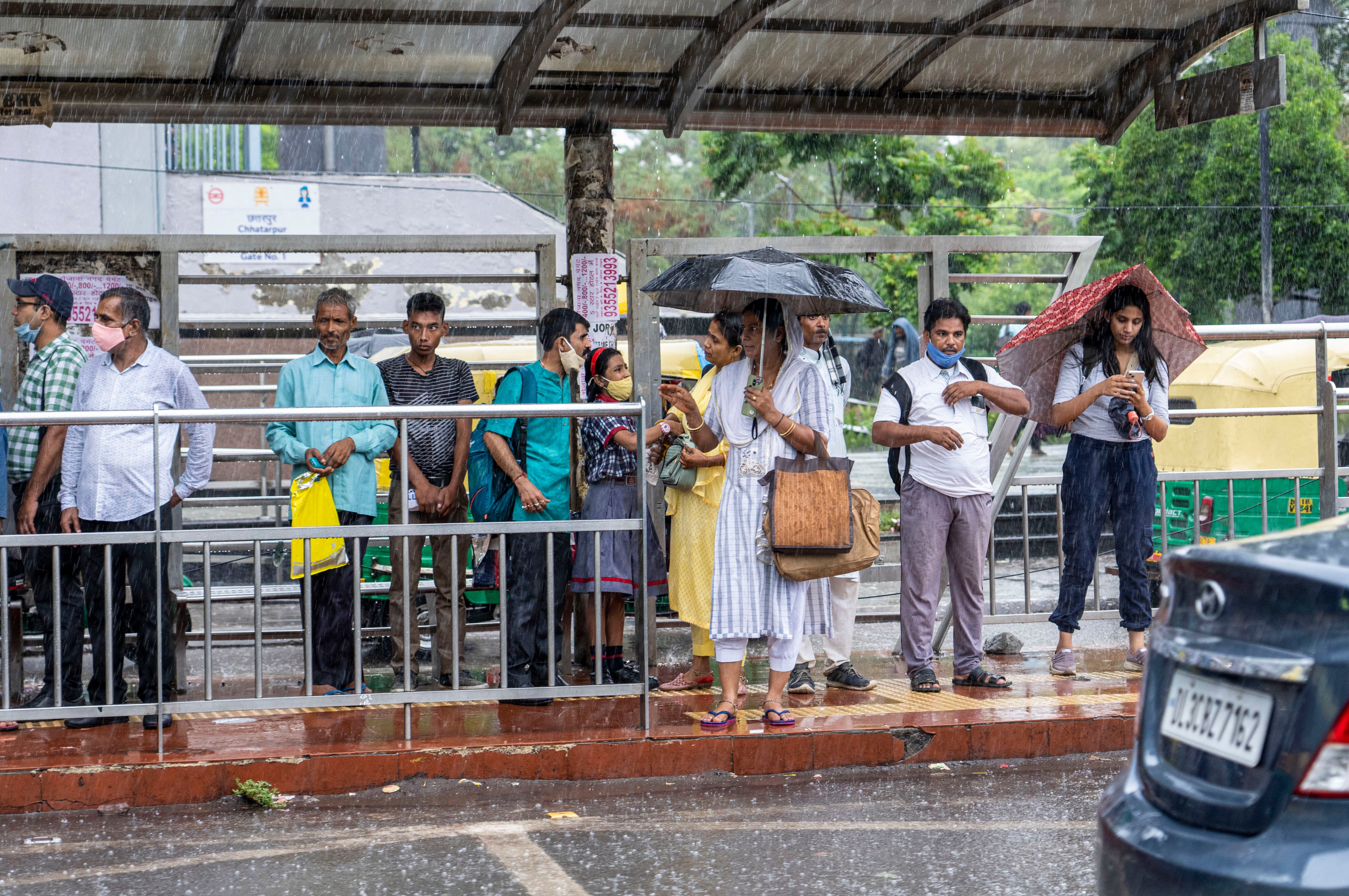 People wait for public transport as it rains in New Delhi