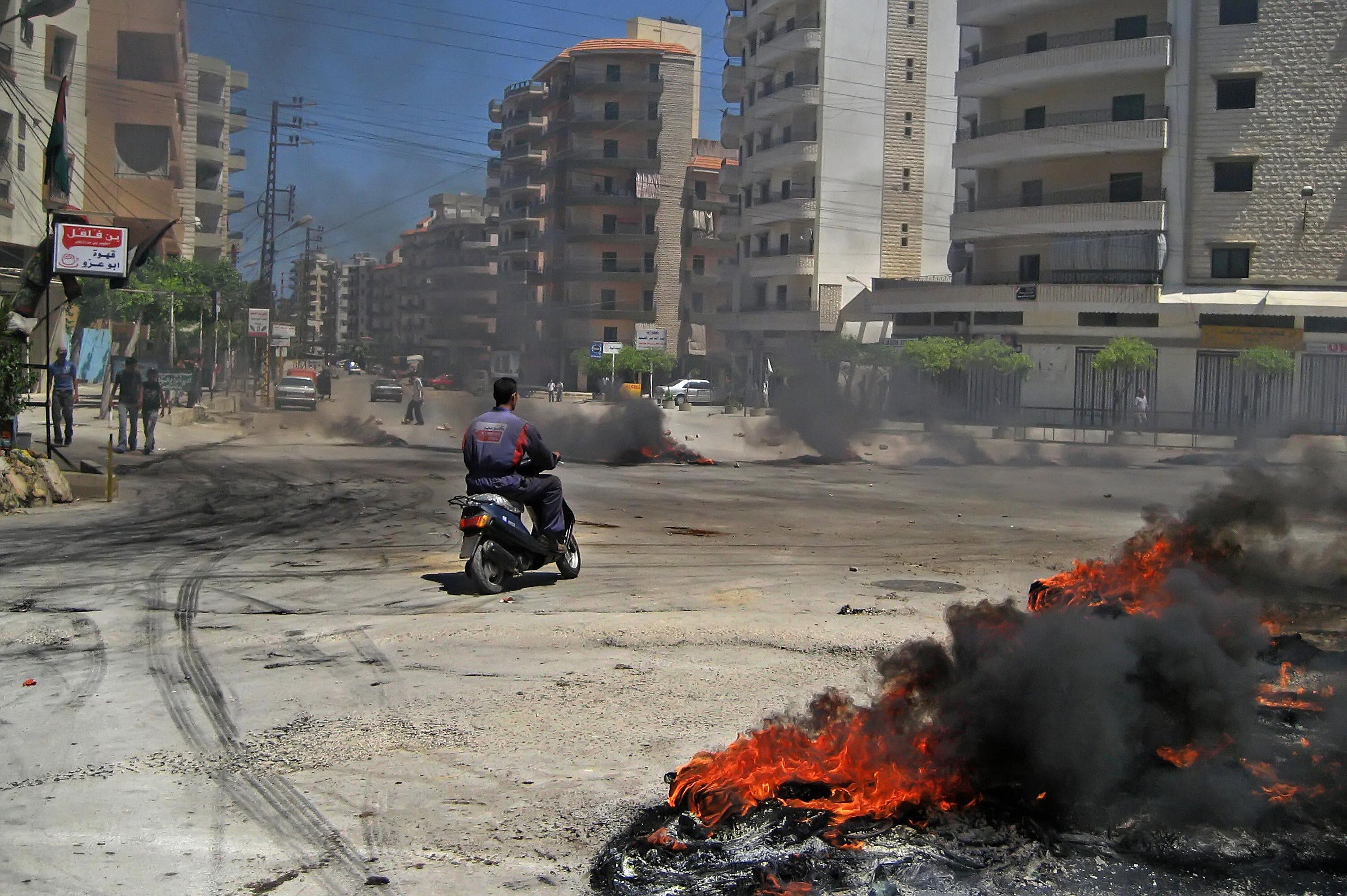 Under fire: in May 2007, a motorcyclist rides past burning tires at the entrance of the Palestinian refugee camp of Bedawi, adjacent to Nahr al-Bared