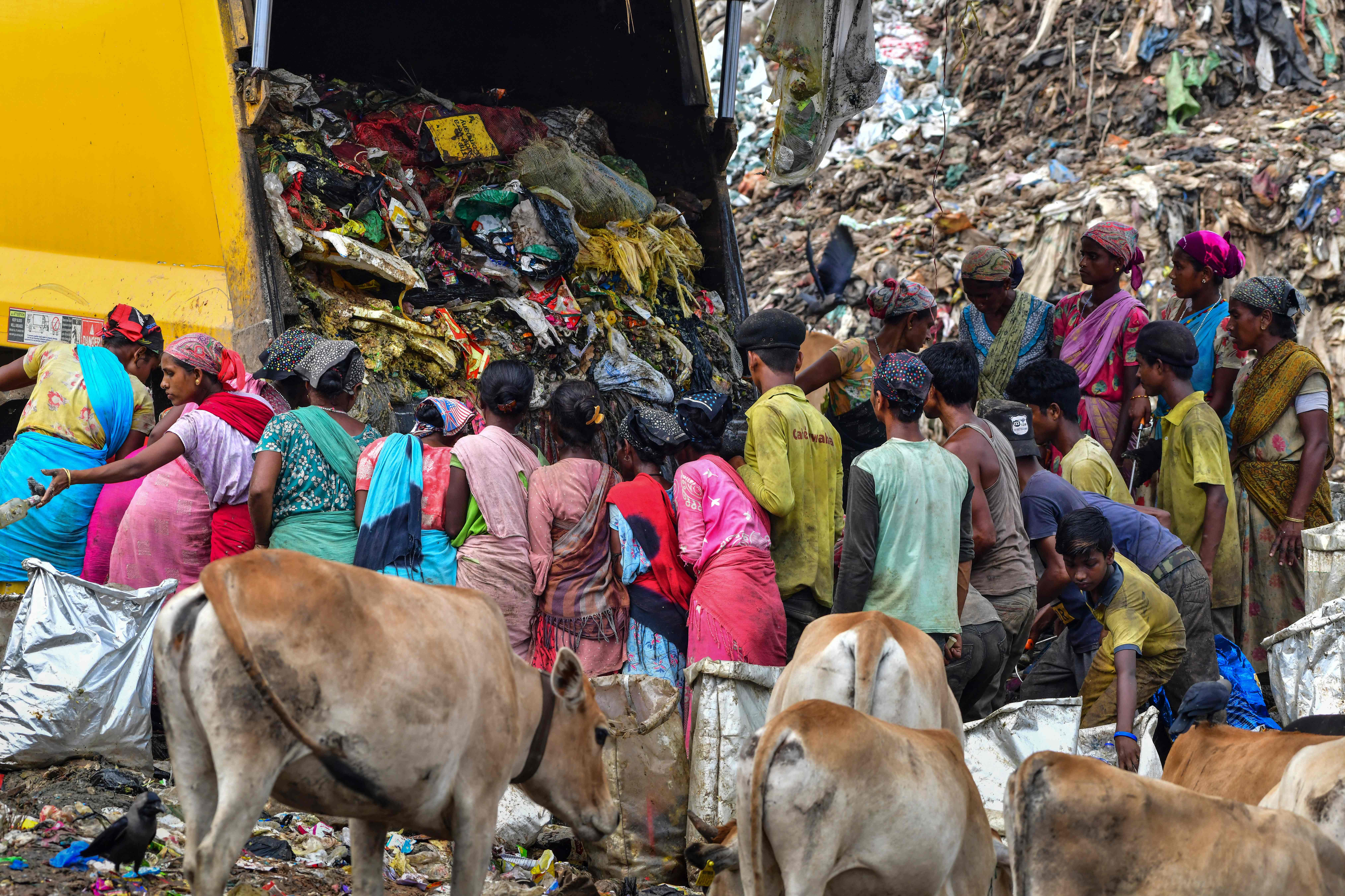 Rag-pickers stand by as a truck unloads rubbish at a dump in Guwahati