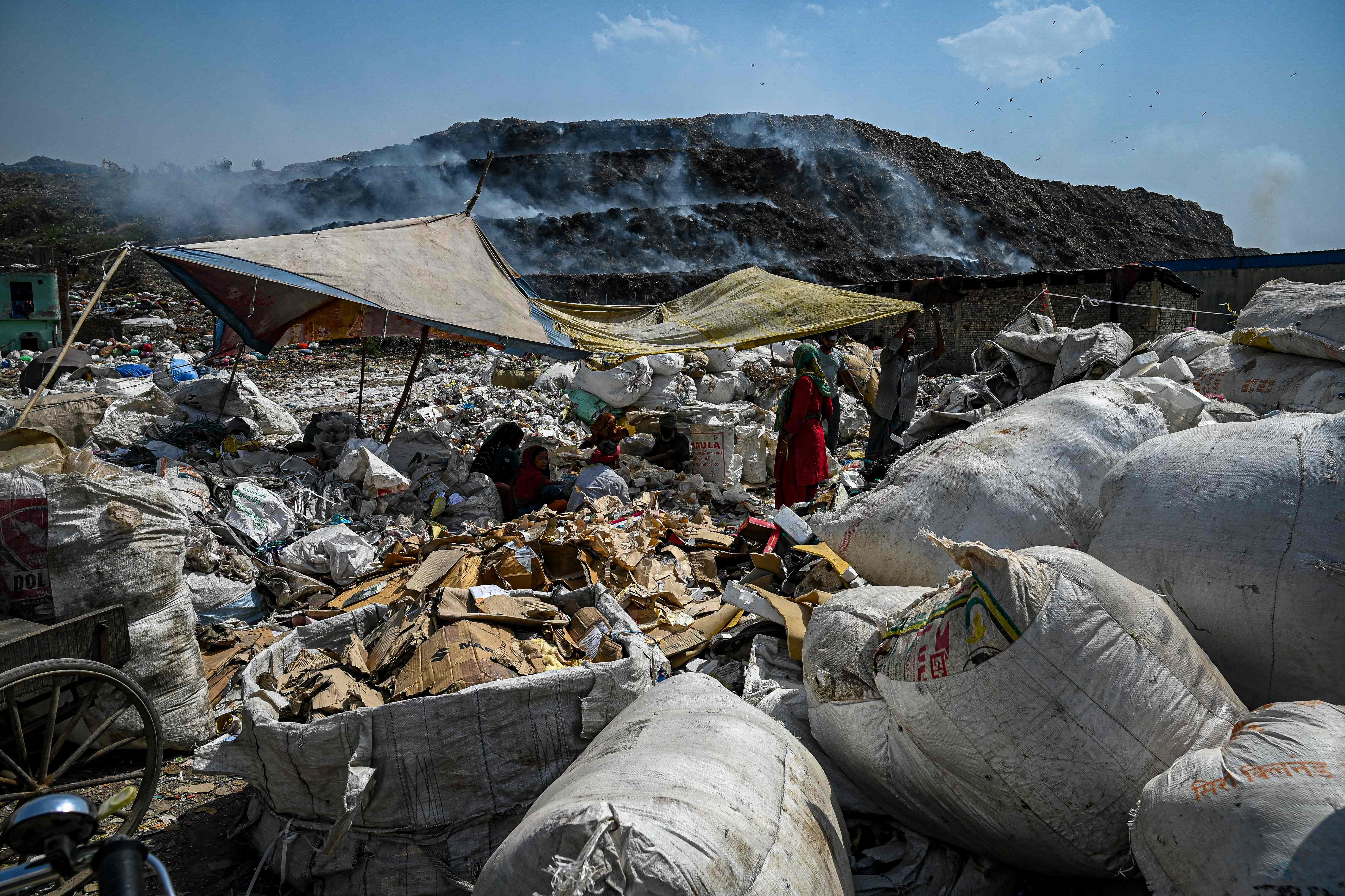 Workers segregate plastic, polythene and other reusable materials from waste collected by ragpickers as smoke billows during a fire at Bhlaswa landfill in New Delhi on 4 June 2022