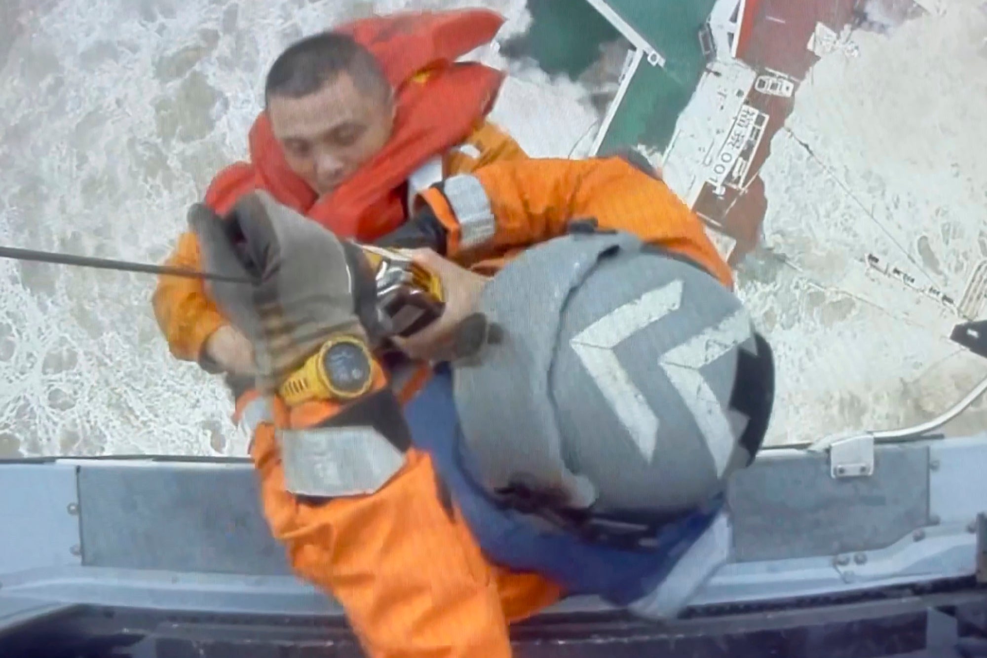 Helicopter crew members winch up a man from a sinking ship in the South China Sea