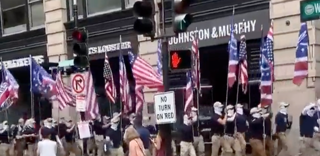 <p>A masked group of white supremacists marches through downtown Boston on 2 July, 2022.</p>