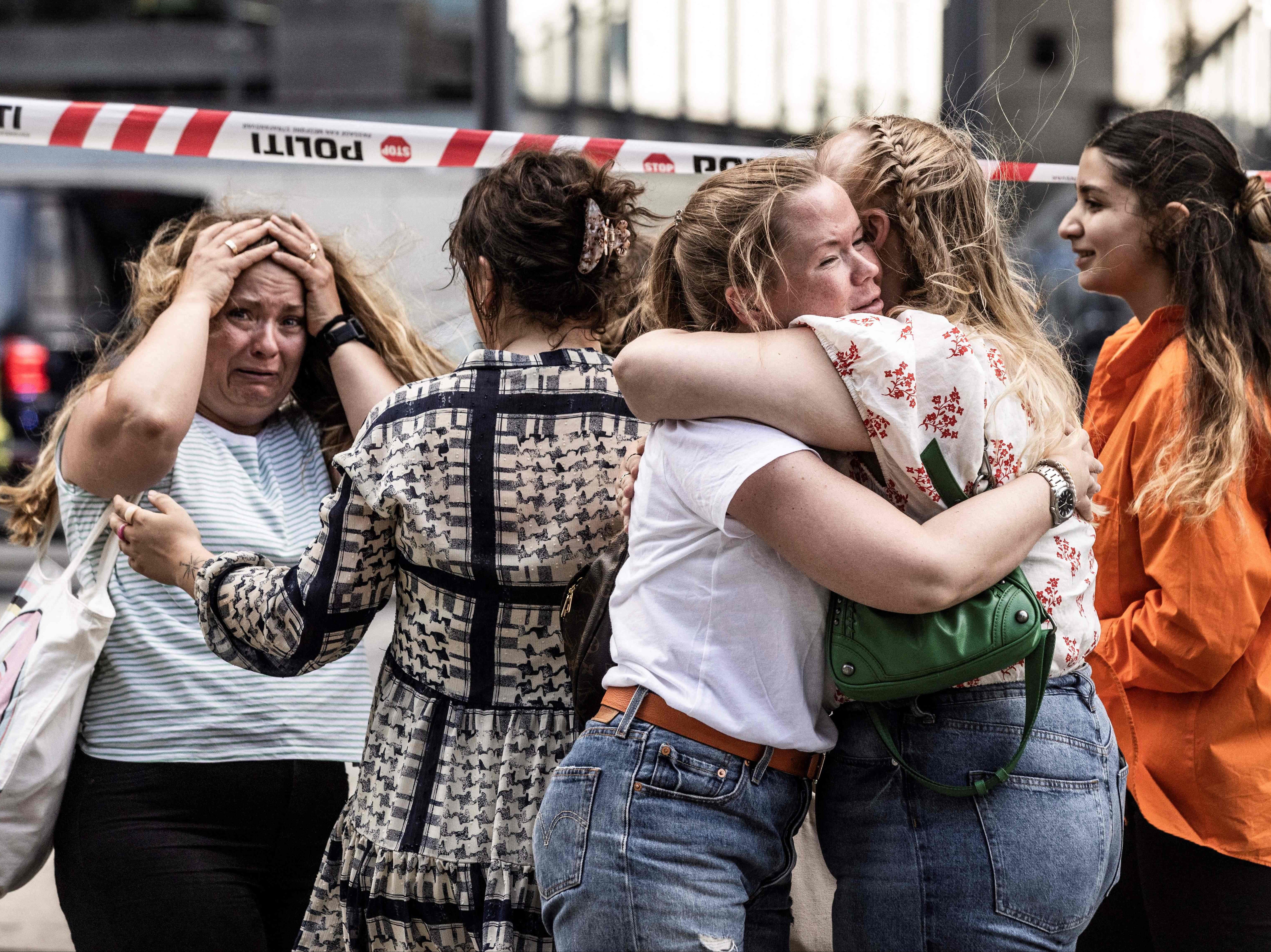 People hug each other outside the Fields shopping mall, where a gunman killed three people and wounded several others