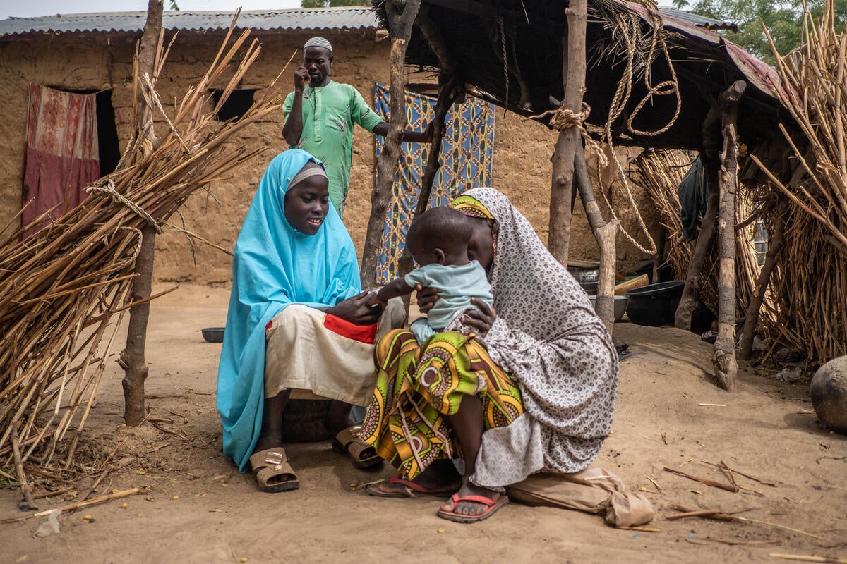 Mallam looks on as Aisha, 30, and Hauwa, 15, play with Bashir, one, outside their home