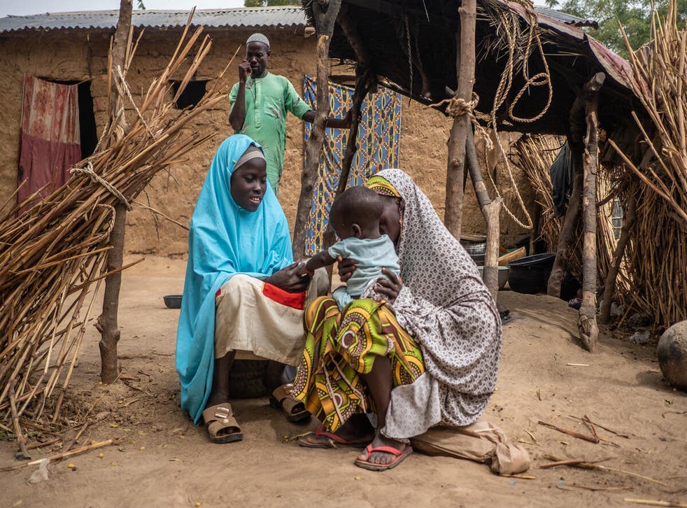 <p>Mallam looks on as Aisha, 30, and Hauwa, 15, play with Bashir, one, outside their home</p>