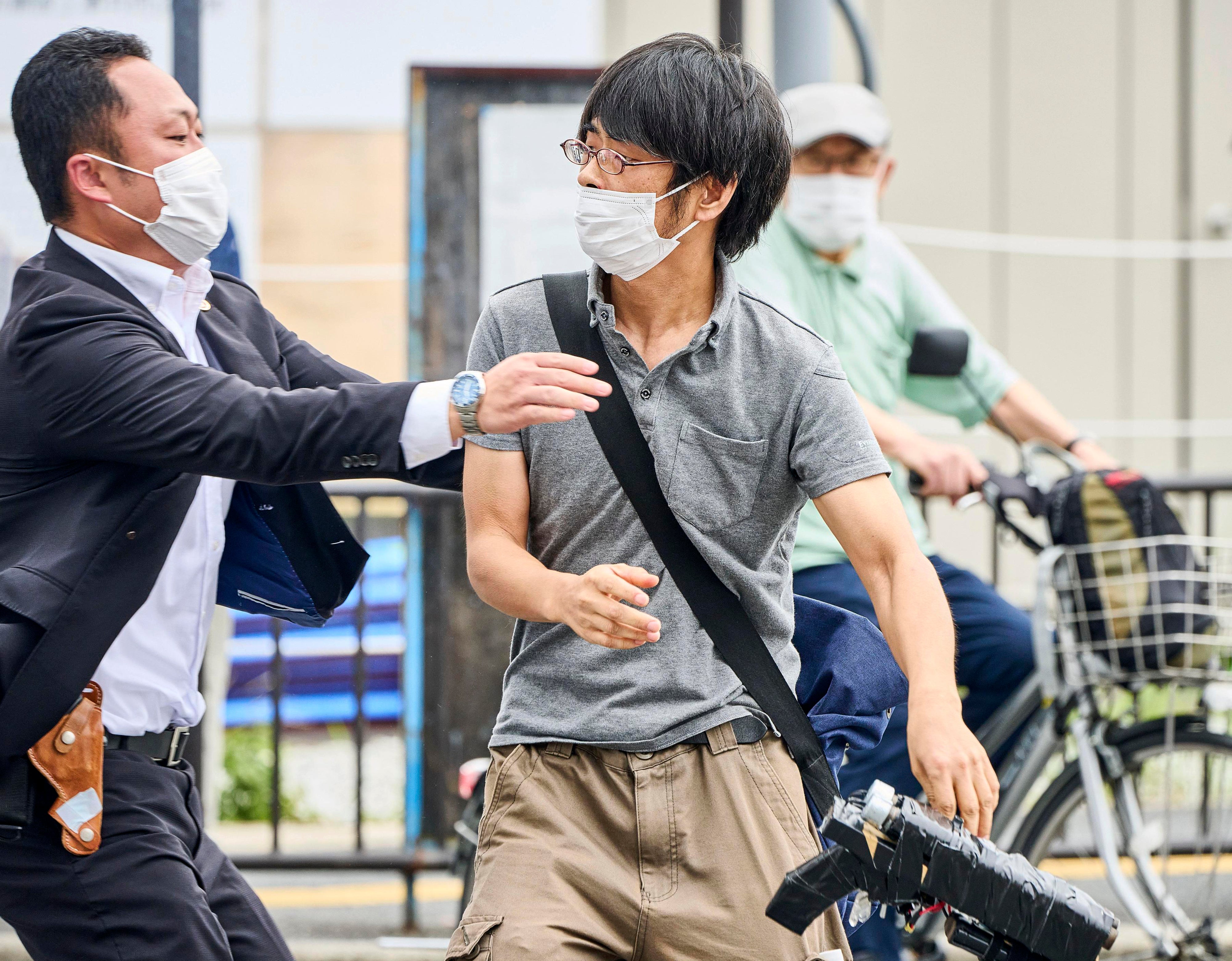 Tetsuya Yamagami (right), suspected of carrying out Shinzo Abe’s assassination has what looks like a ‘homemade’ weapon slung on his shoulder and is being detained near the site of gunshots in Nara, western Japan Friday, 8 July 2022