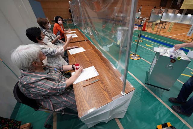 <p>Staff members of a local election administration commission, wearing face masks, observe a voter cast a ballot in the upper house elections at a polling station Sunday, 10 July 2022, in Tokyo</p>