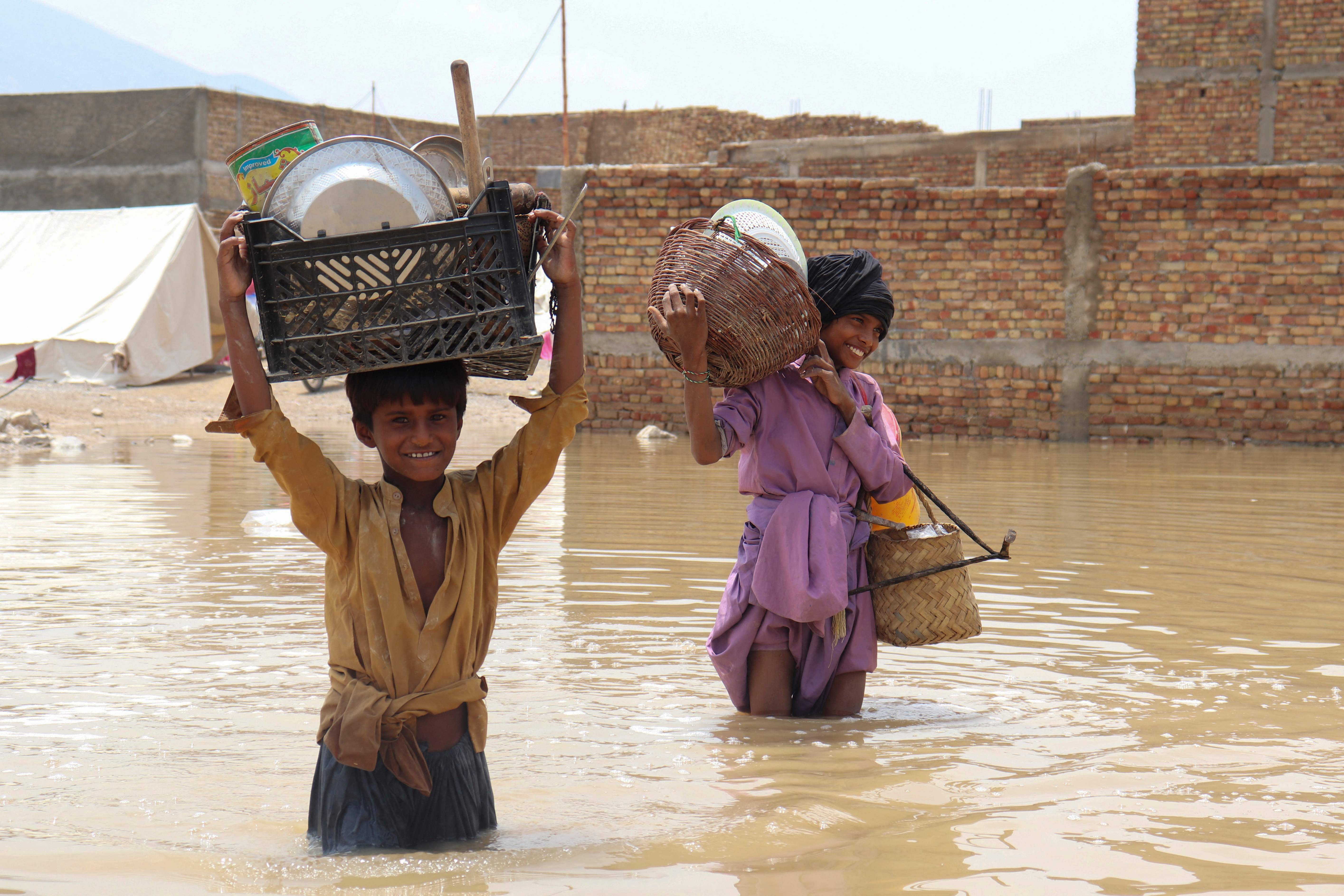 Children carrying household items wade through a flooded area after a monsoon rainfall in Quetta