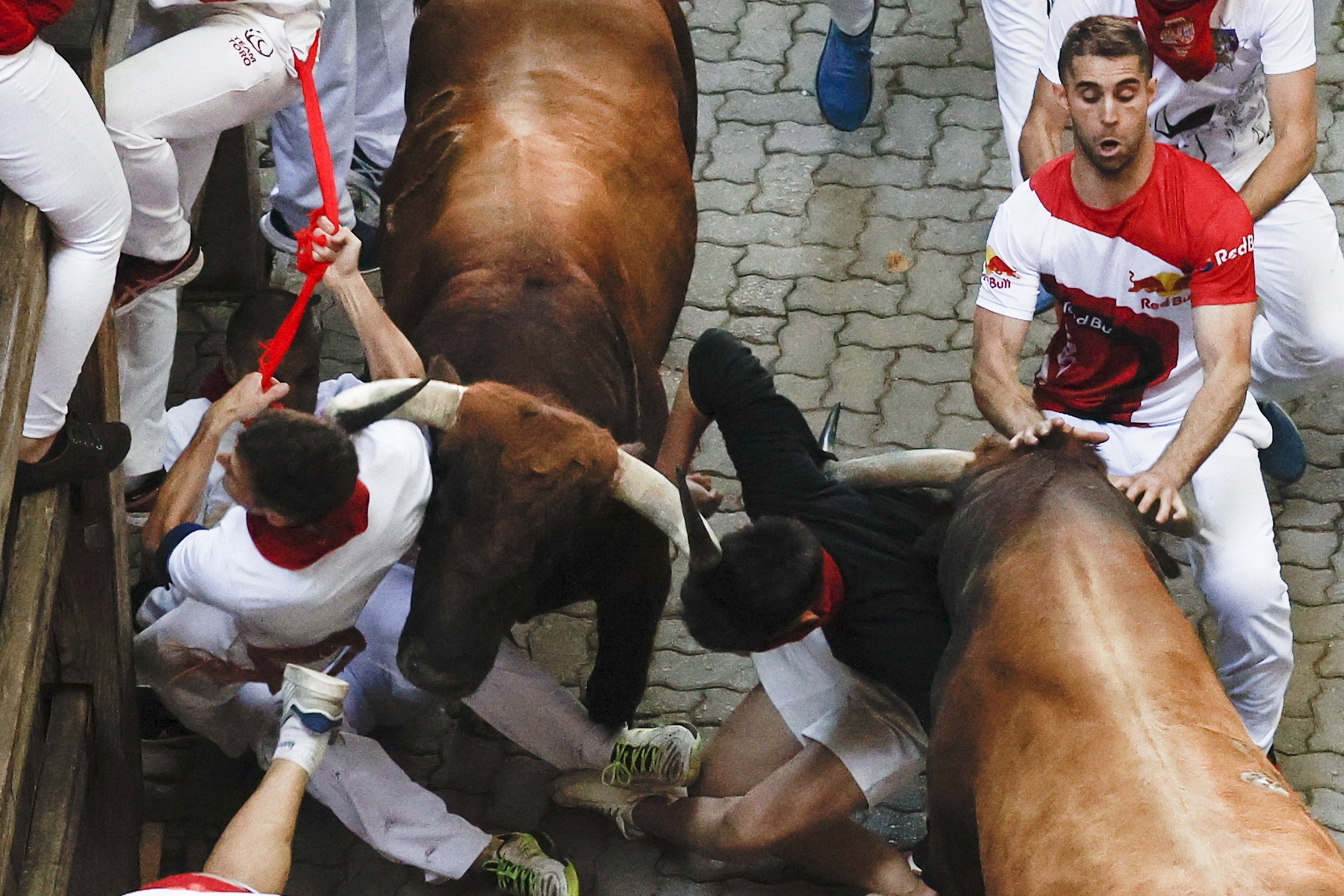 People try to avoid a bull during the fifth ‘encierro’ or running of the bulls during the San Fermin Festival