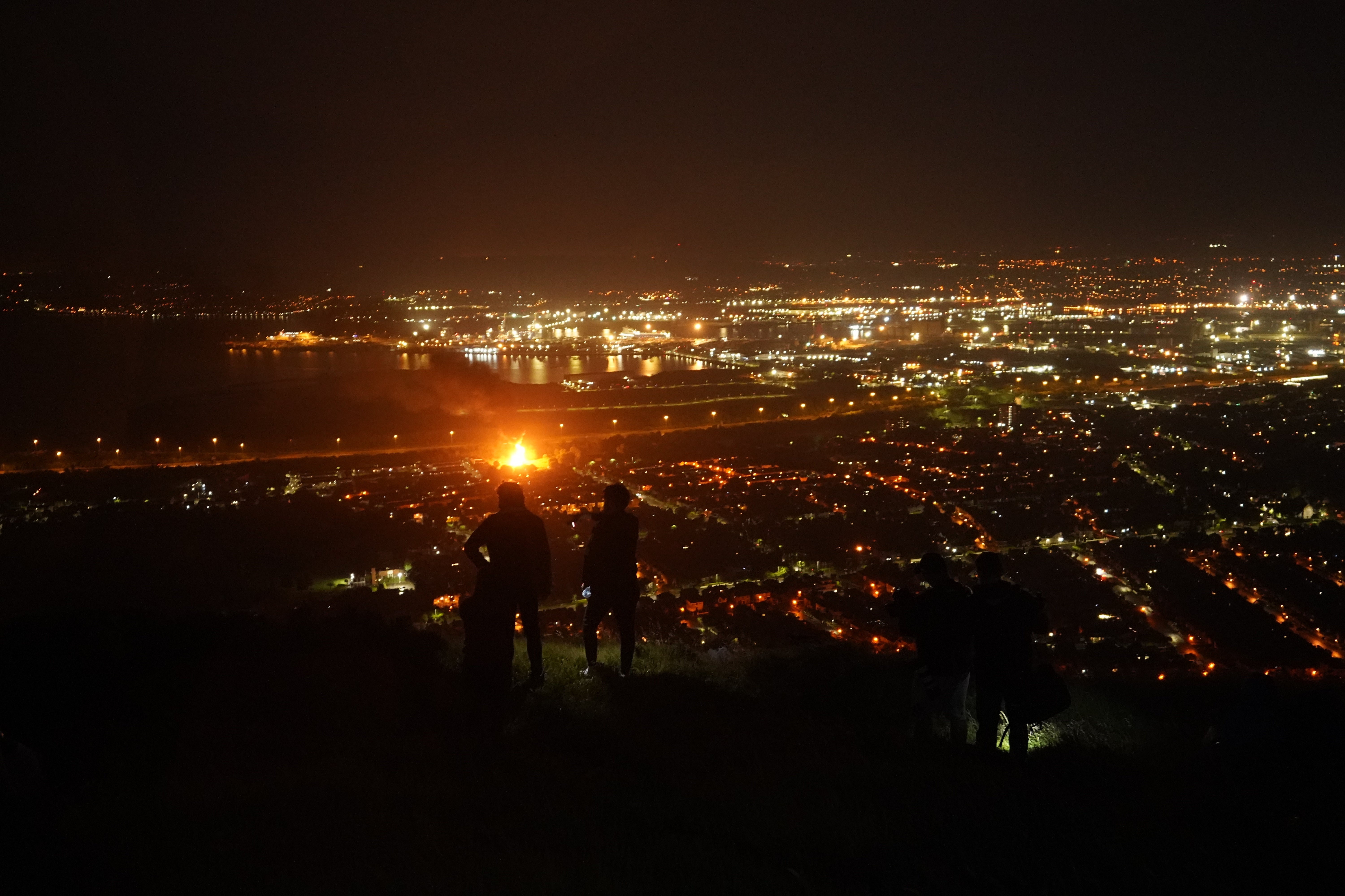 People stand on Cavehill in Belfast as they watch bonfires being lit across the city on the ‘Eleventh night’ to usher in the Twelfth commemorations (Niall Carson/PA)