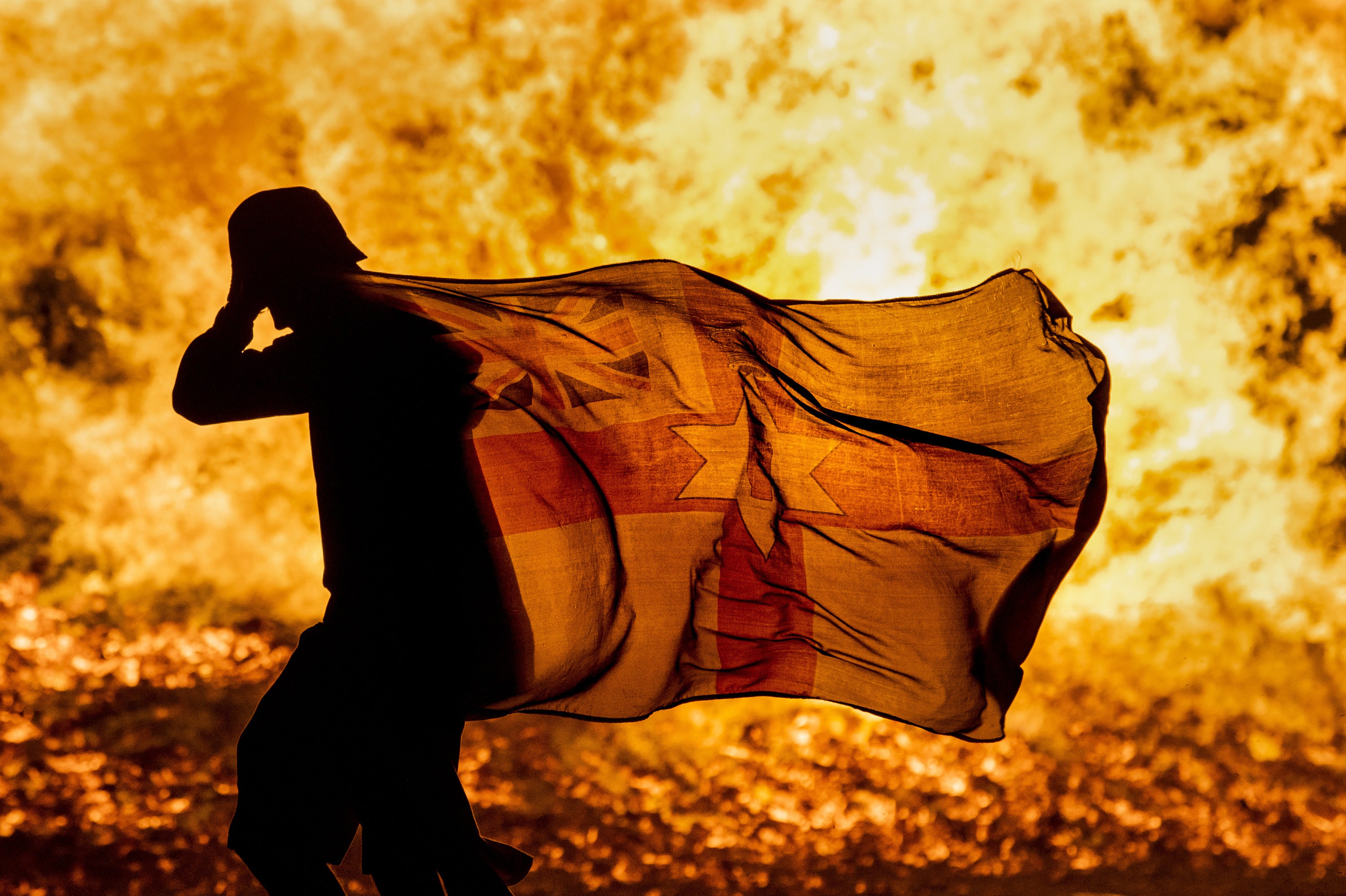 A young man carries a Northern Ireland flag in silhouette past the burning Craigyhill loyalist bonfire in Larne, Co Antrim, on the Eleventh Night (Liam McBurney/PA)