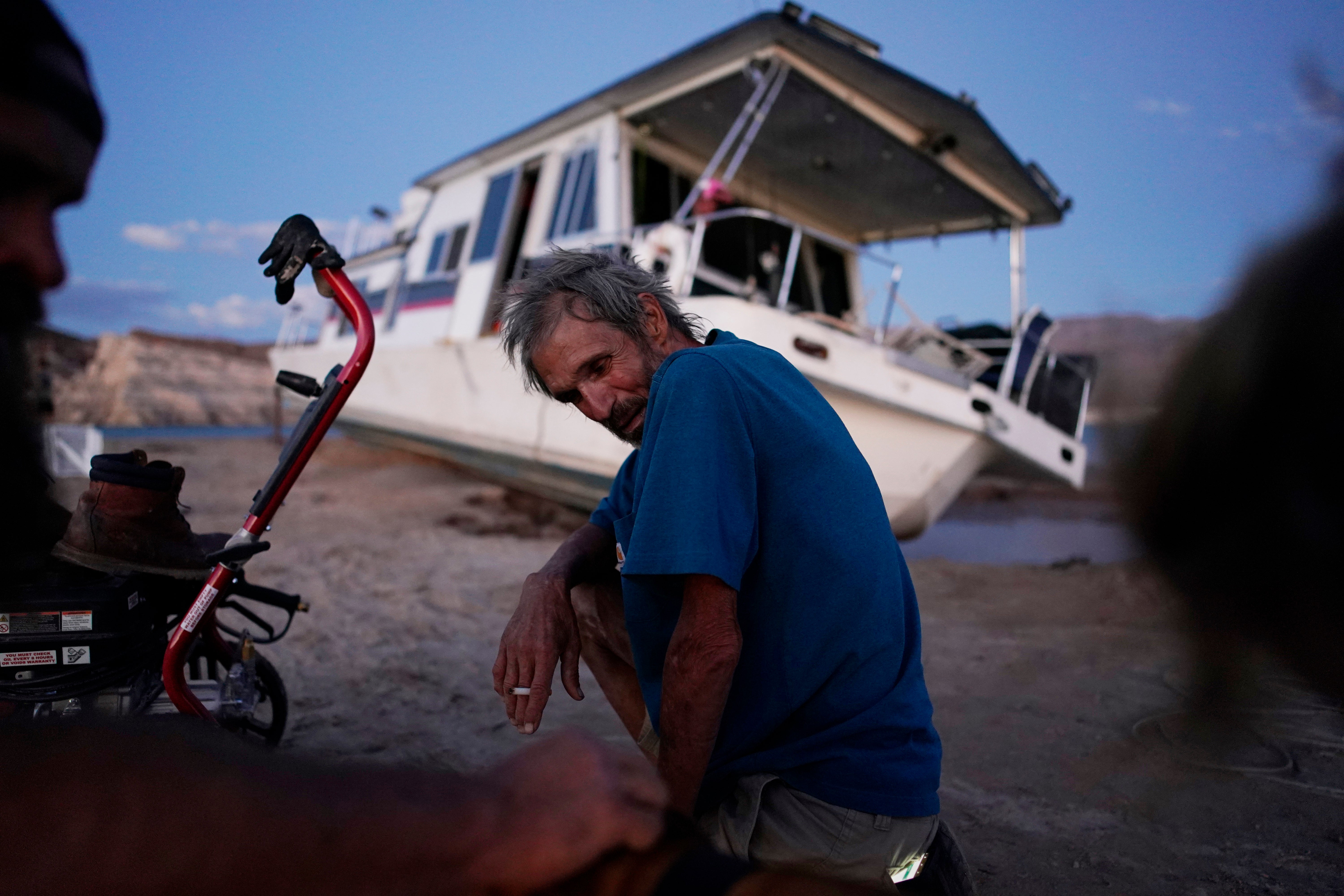 A man sits near his beached houseboat on the shore of Lake Mead