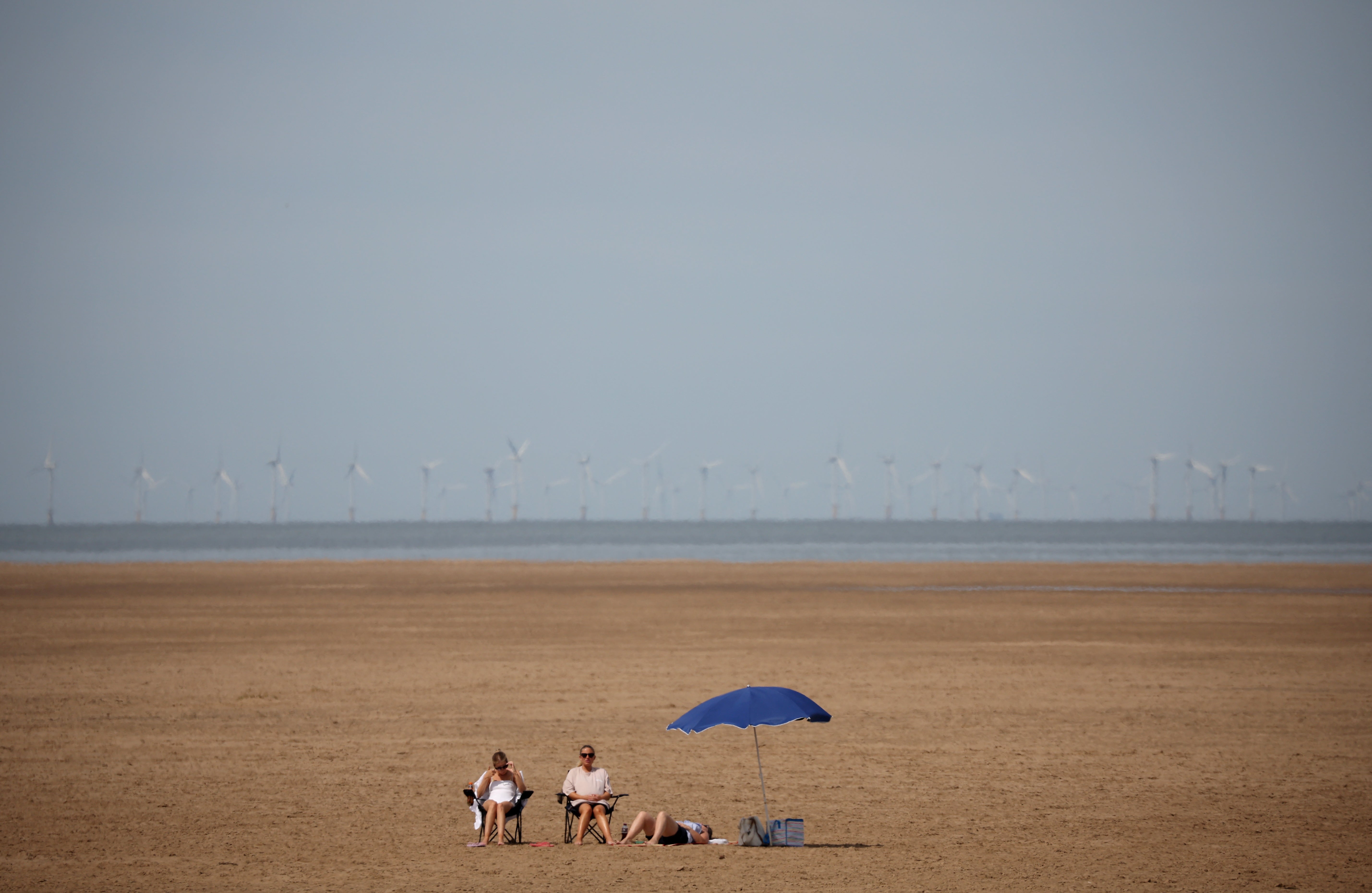 People sit on deckchairs on an empty beach in Hoylake on the Wirral