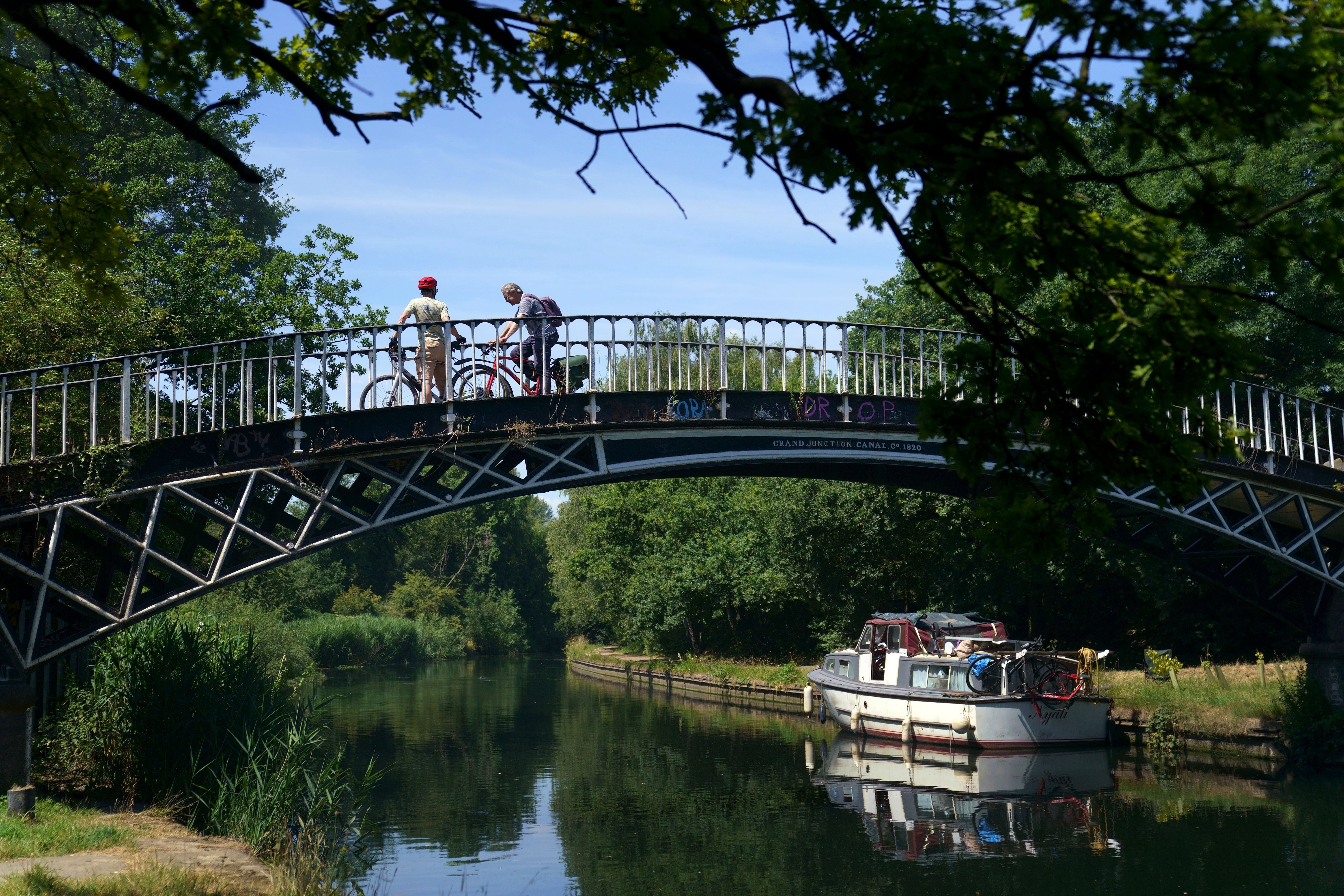 A pair of cyclists cross a bridge over the River Brent