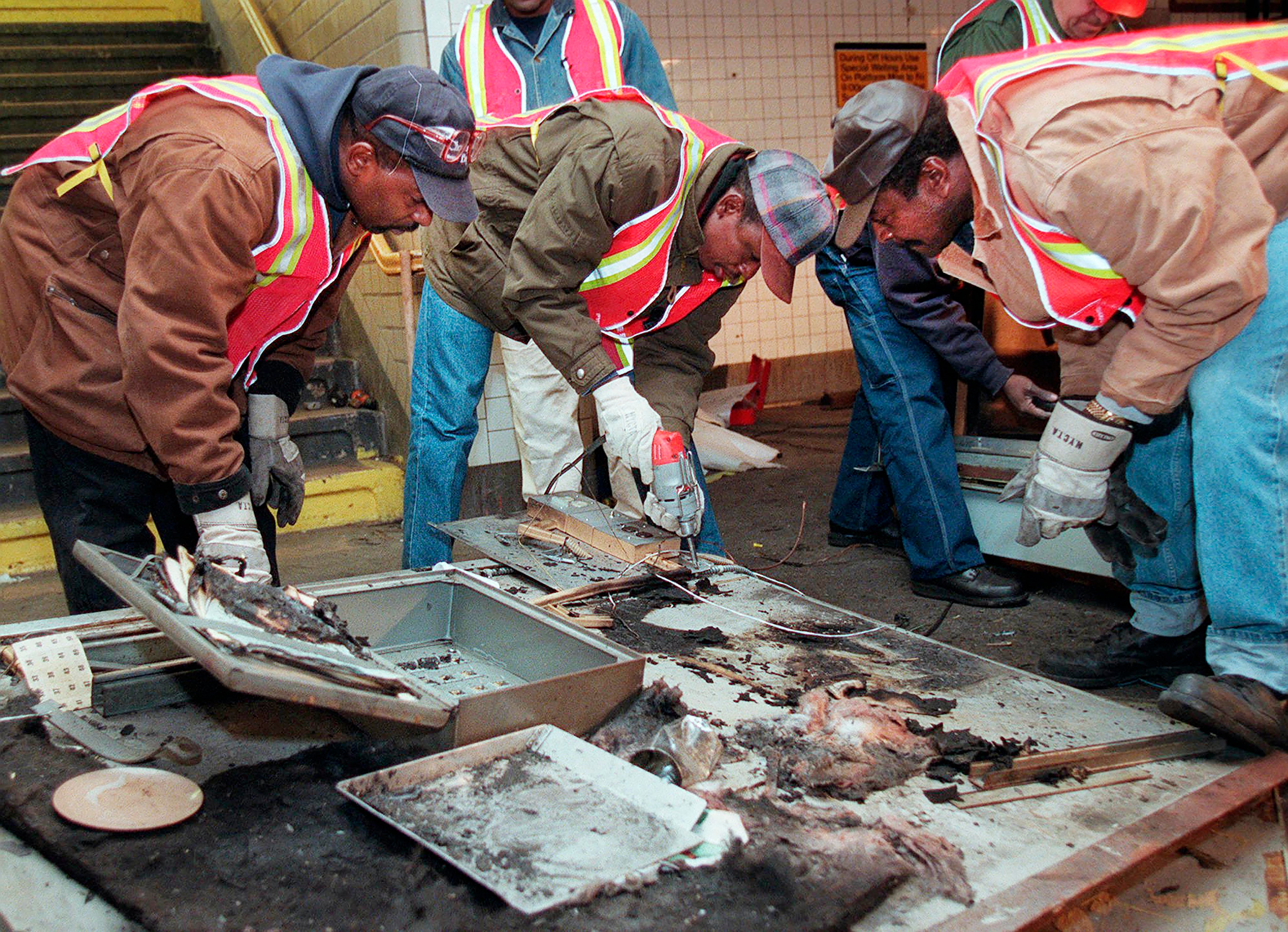 Transit workers dismantle the charred inner wall of a token booth at the Kingston Avenue and Fulton Street subway station in the Bedford-Stuyvesant section of Brooklyn, November 26, 1995, after attackers sprayed a flammable liquid into the token booth and set it on fire