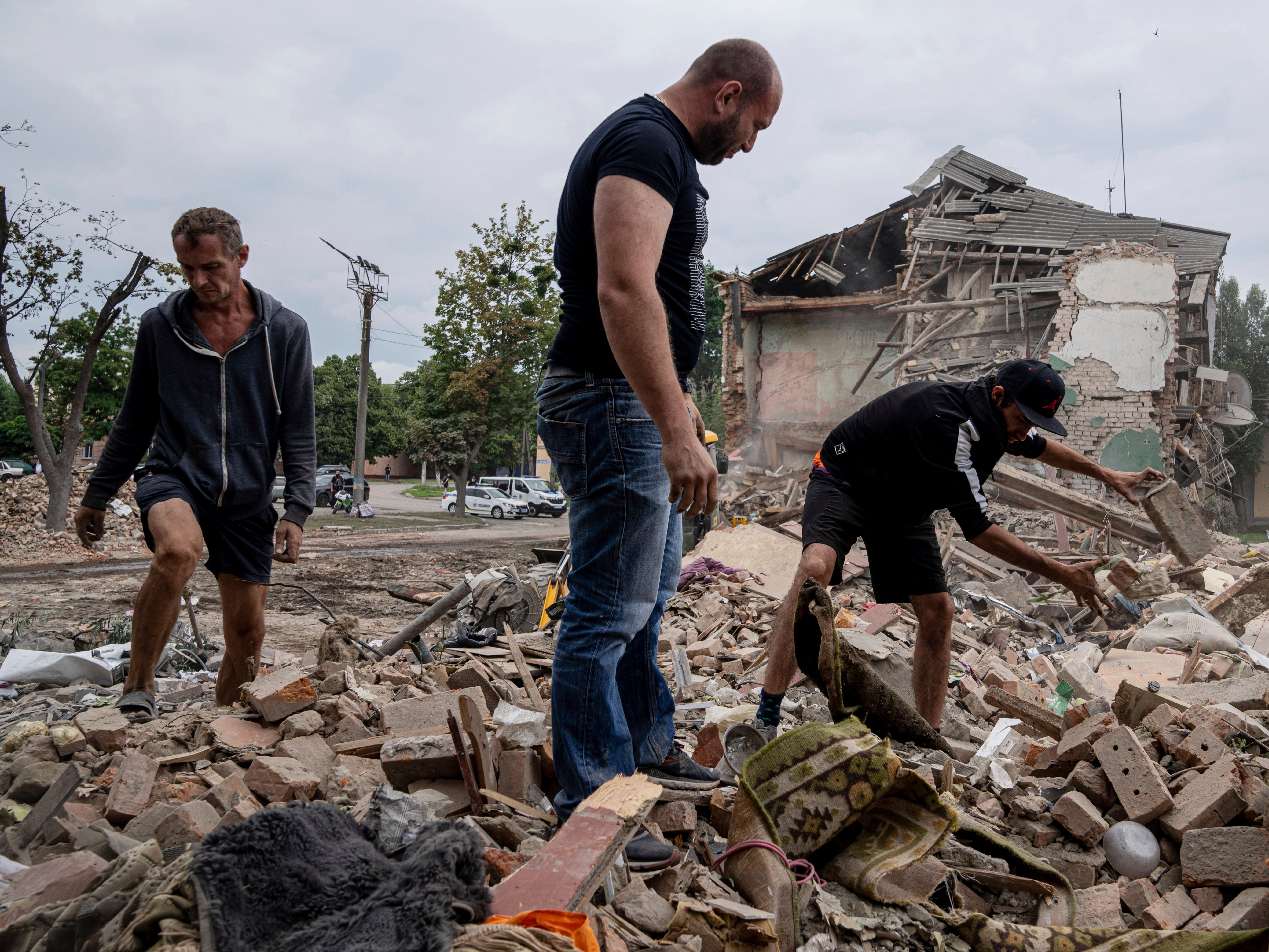 Local residents search for documents of their injured friend in the debris of a destroyed apartment house after Russian shelling in a residential area in Chuhuiv