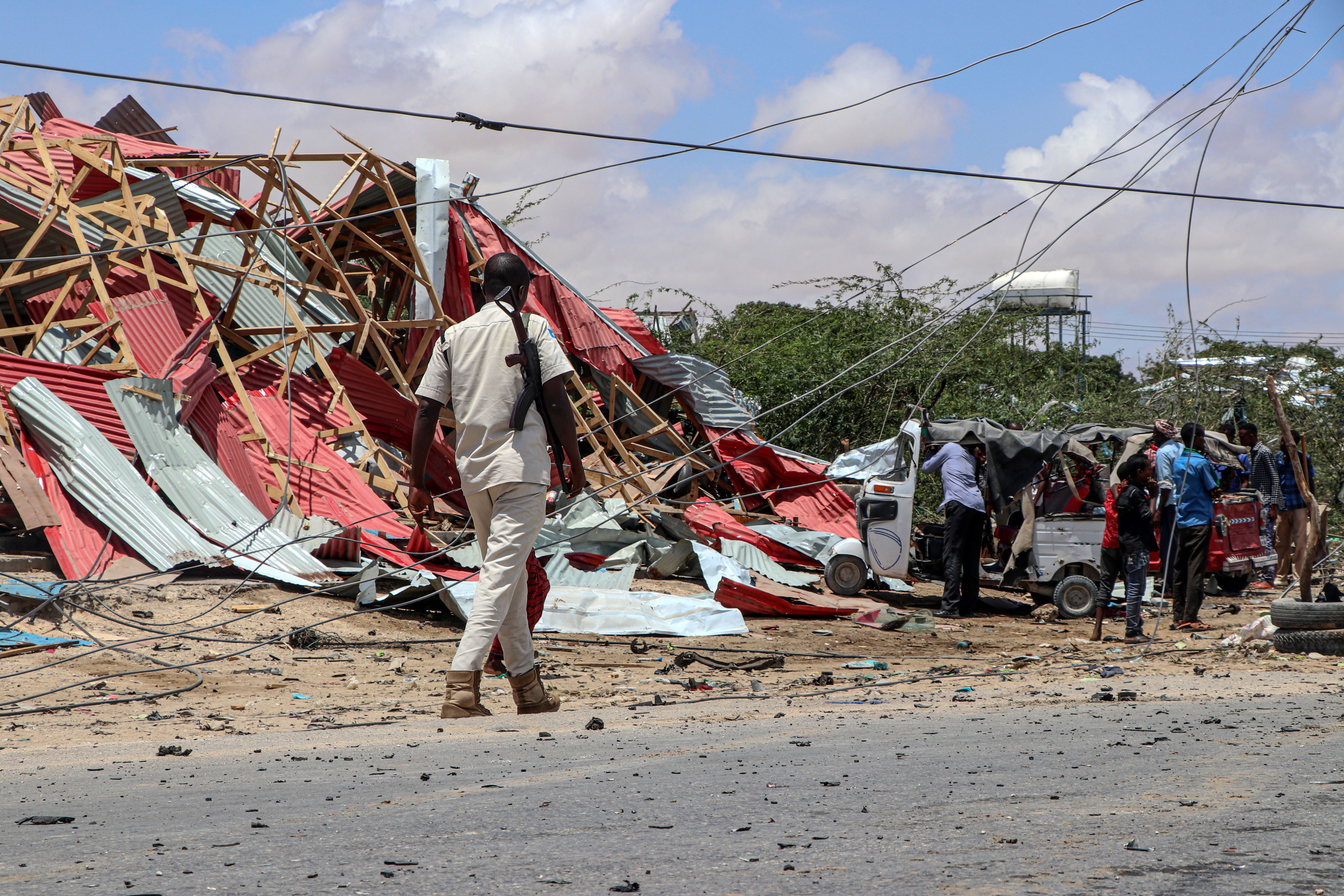 A Somali police officer patrols as bystanders gather at the site of a suicide car bomb explosion that targeted a European Union vehicle convoy in 2019