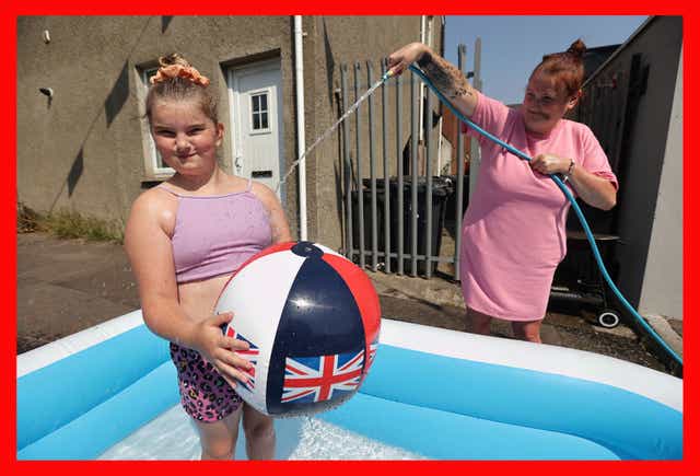 Danielle Lofthouse cools down her daughter Amelia Bradford, 10, with a hose as they enjoy the hot weather off the Shankill Road in Belfast (Liam McBurney/PA)