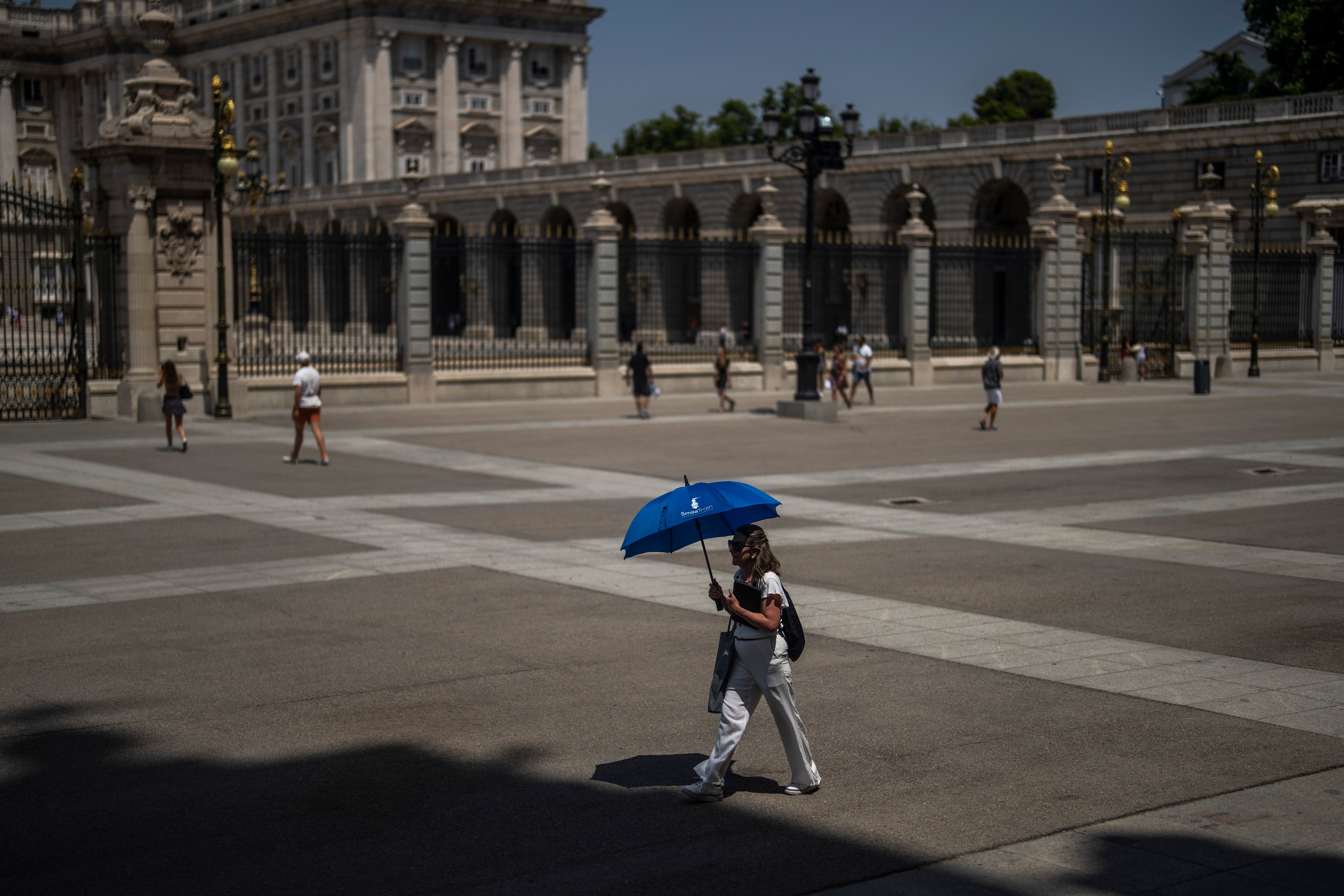 A woman shelters from the sun with an umbrella in front of the Royal Palace in Madrid