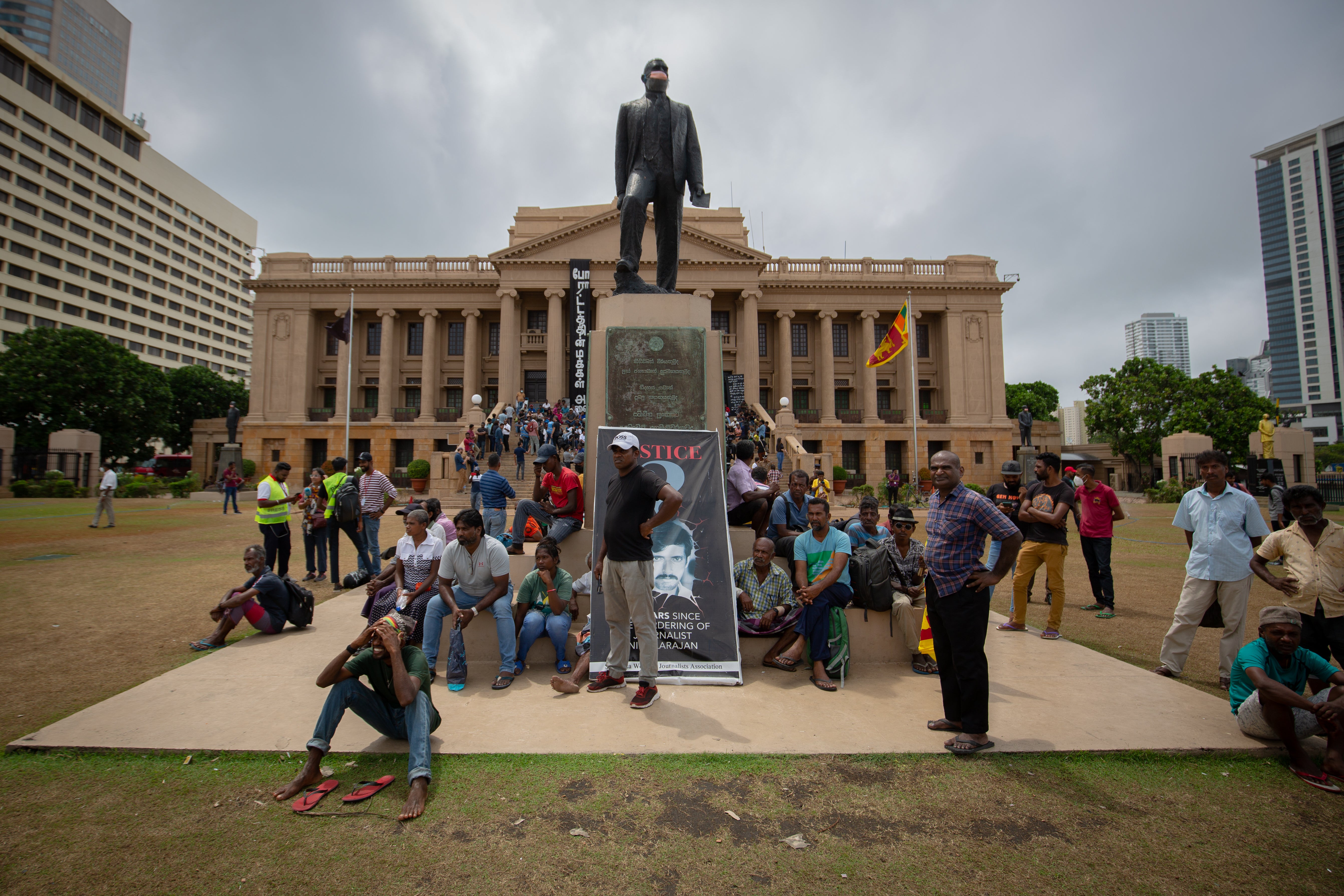 People sit beneath the statue of Don Stephen Senanayake, the first Prime Minister of independent Ceylon, to watch parliamentary proceedings being shown on a giant screen on the lawns of the Presidential Secretariat on 20 July 2022 in Colombo, Sri Lanka