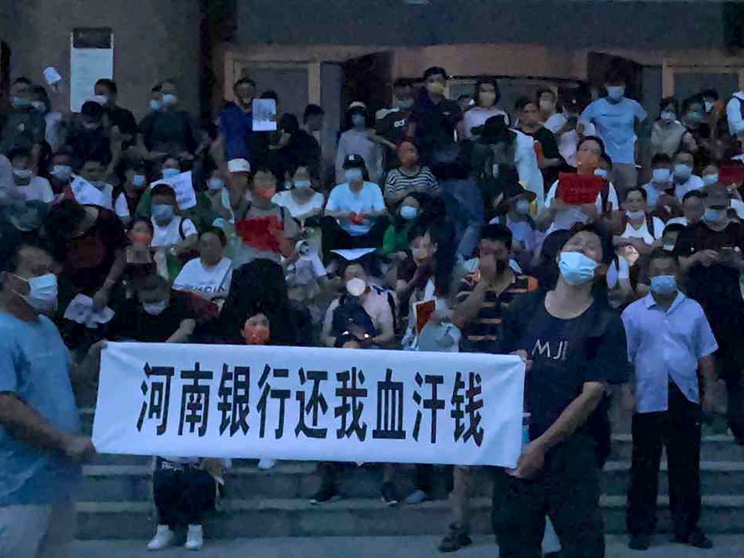 People hold banners and chant slogans stage a protest at the entrance to a branch of China's central bank in Zhengzhou in central China's Henan Province