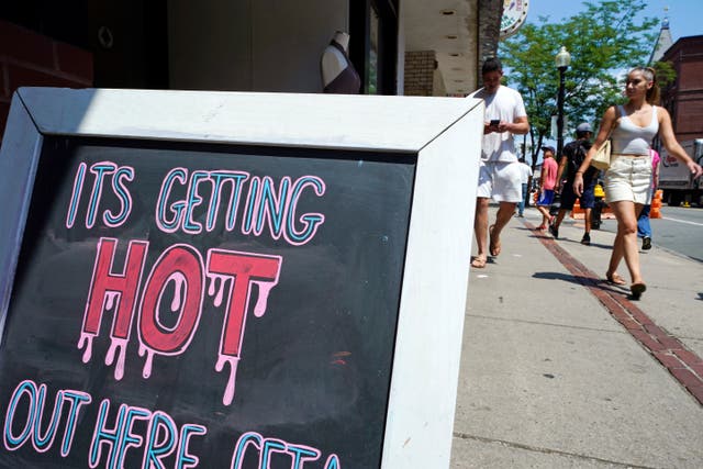 <p>With temperatures hovering in the mid 90s, people walk near a sign down Hanover Street in the North End, during a summer heatwave</p>