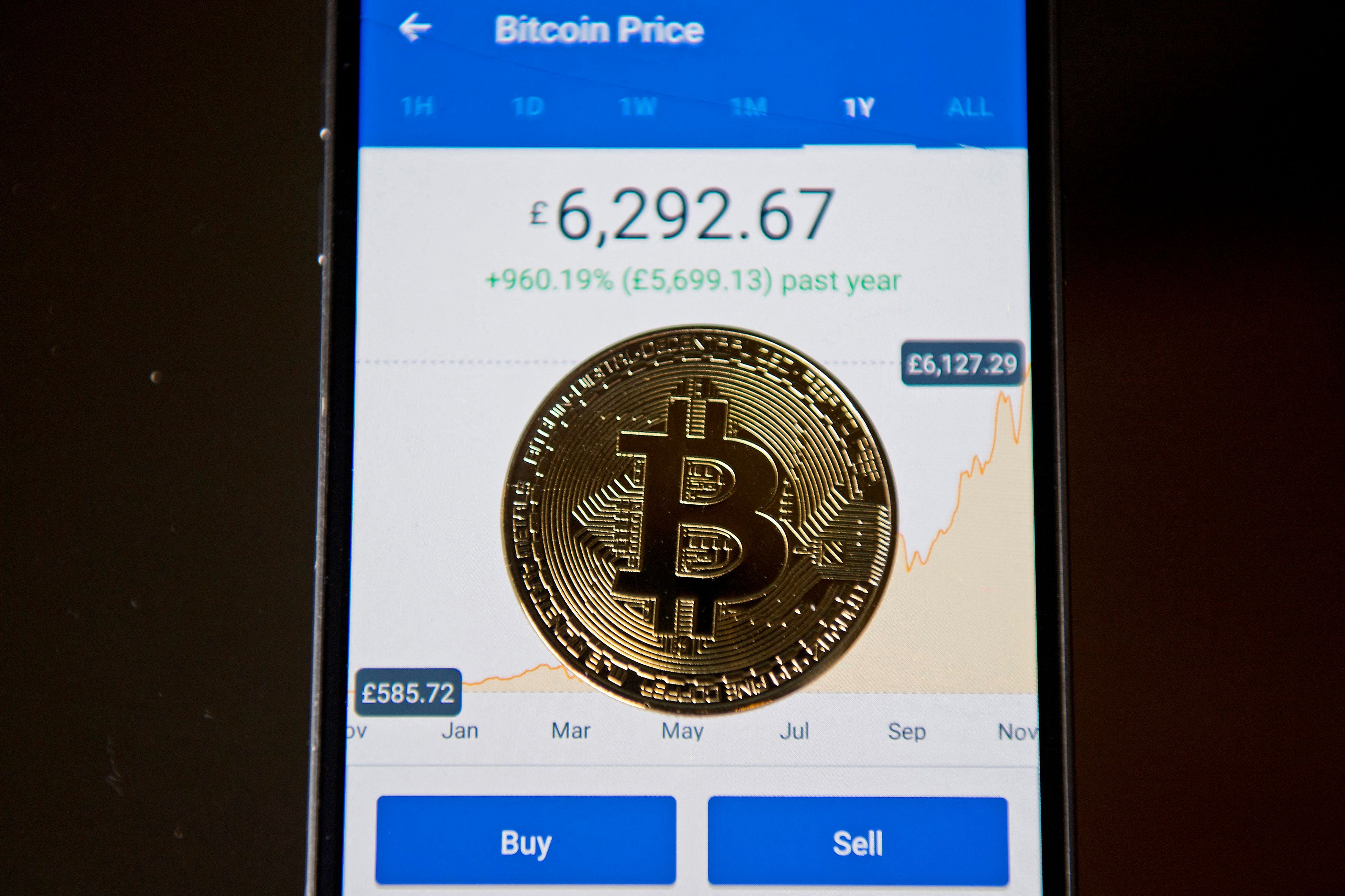 A gold plated souvenir Bitcoin coin is arranged for a photograph on a smart phone displaying current value of a single bitcoin, and options to buy or sell, on an app for the digital asset broker, Coinbase, in London on November 20, 2017. (Photo by JUSTIN TALLIS/AFP via Getty Images)