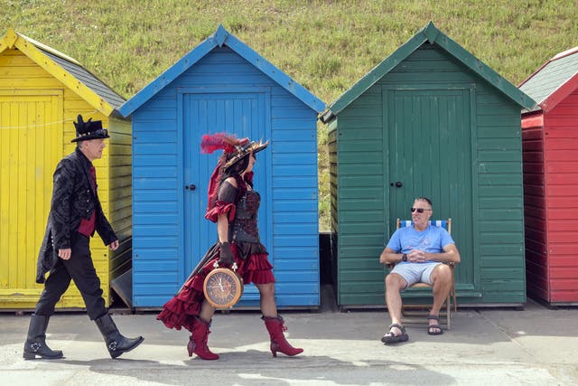 Karen and John Austin walk past a sunbather as they attend the Whitby Steampunk Weekend (Danny Lawson/PA)