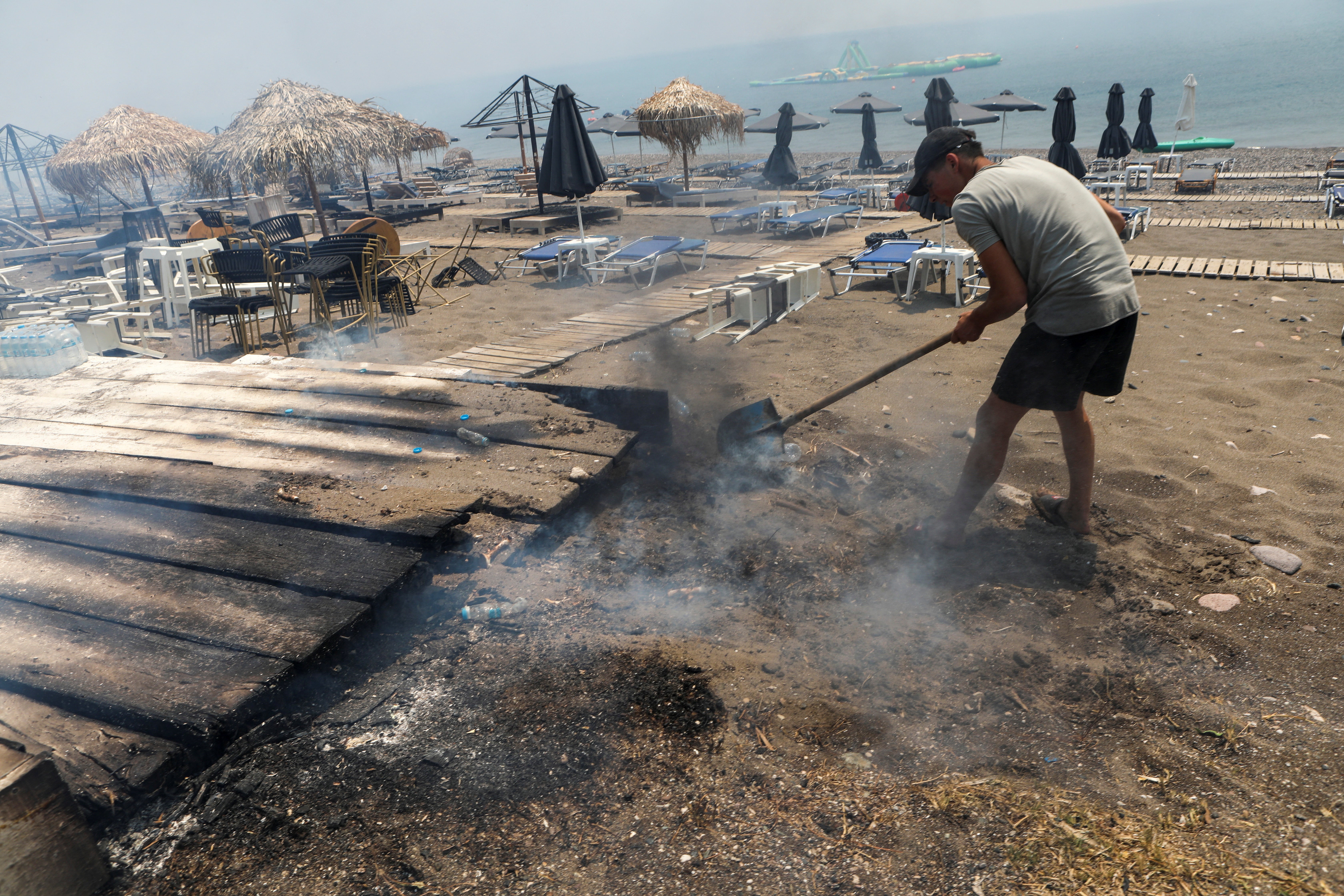 A local puts out flames at a damaged beach bar as wildfire burns near Vatera