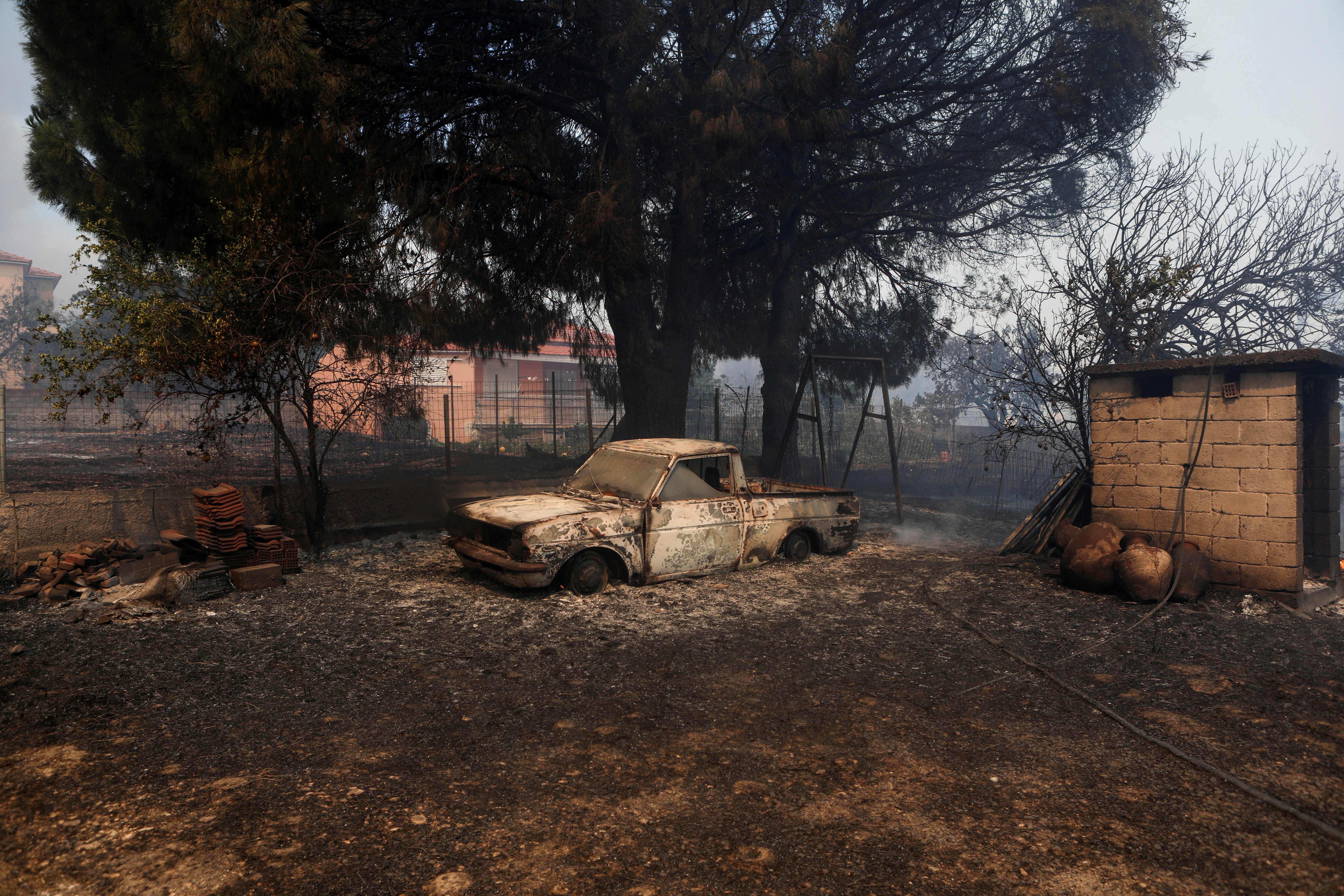 A burned car is seen in a yard as a wildfire rages in Vatera