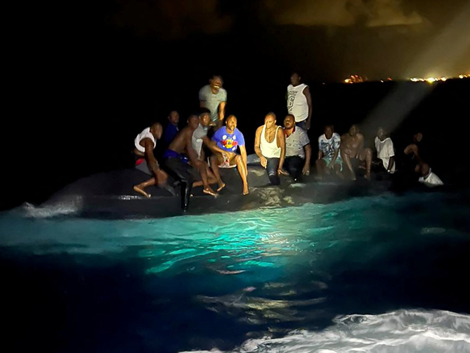 Survivors of a migrant boat that capsized perch on the overturned vessel off the coast of New Providence island