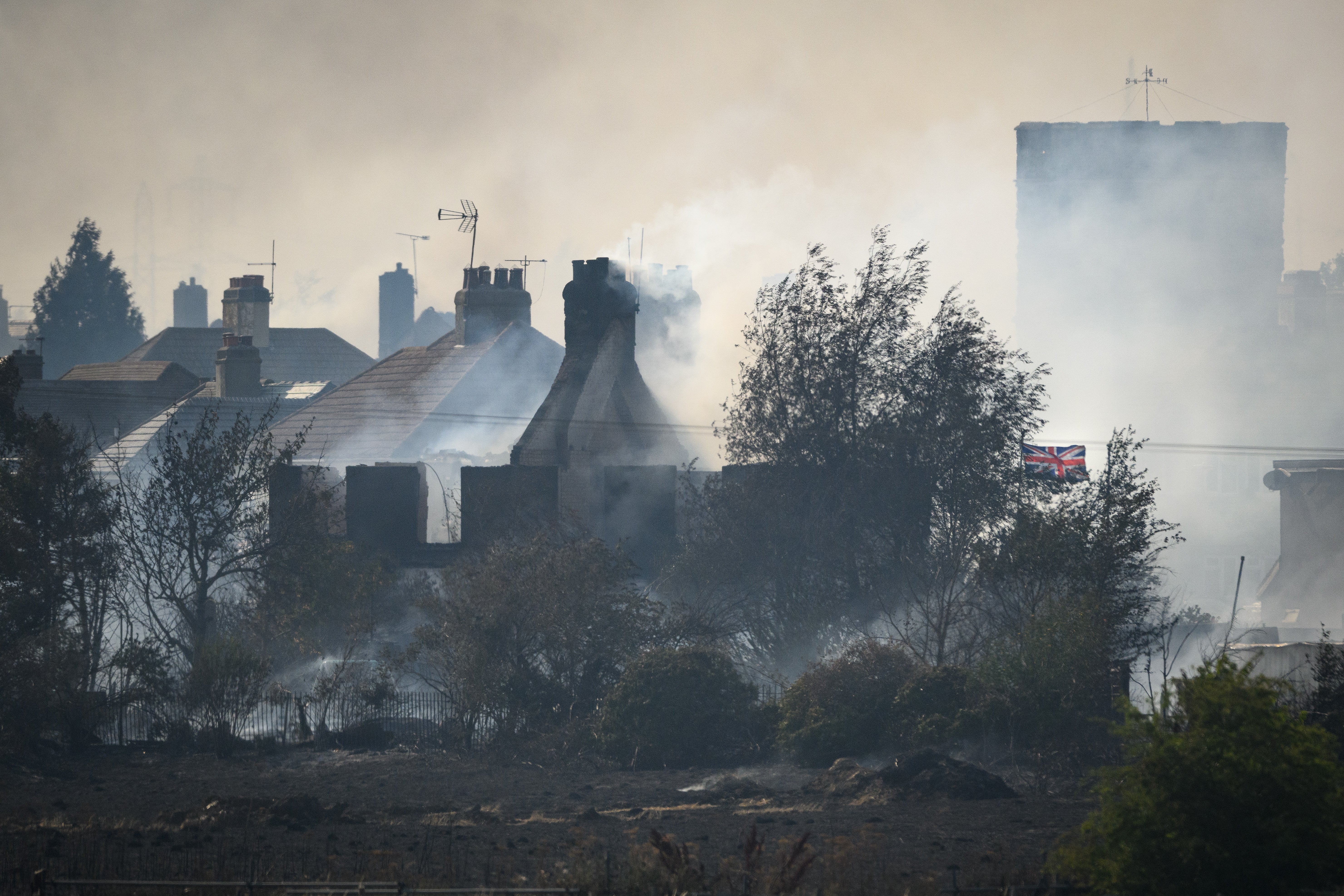 A Union Flag flies amongst the smouldering ruins of houses as fire services tackle a large blaze on July 19, 2022 in Wennington, England.