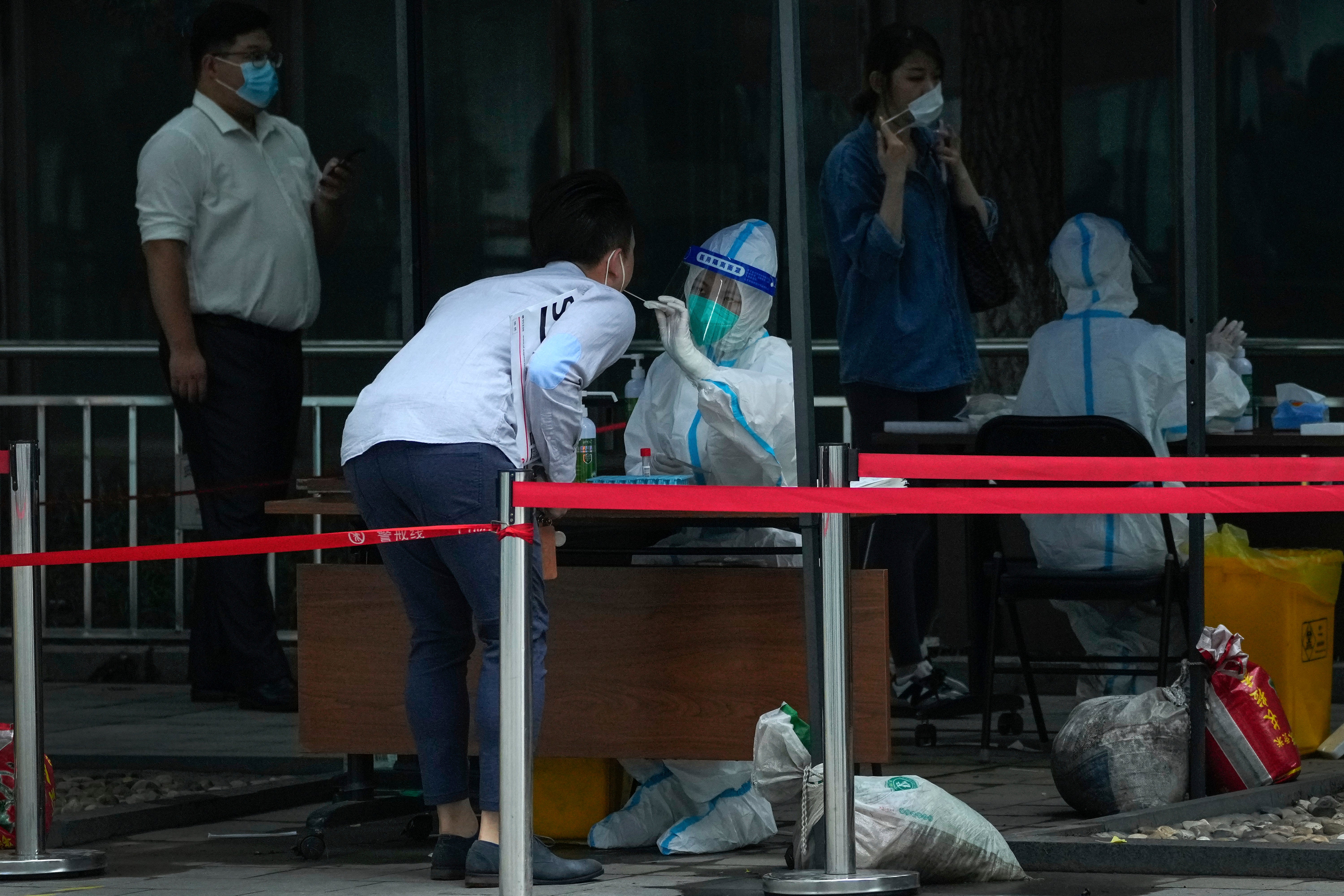 Office workers line up to get their routine throat swab at a COVID-19 testing site in Beijing, Wednesday