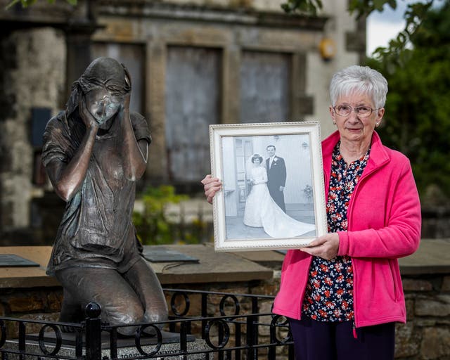 Anne Bradley, whose husband Arthur Hone known as Artie Hone, was one of nine killed in the Claudy bombings in 1972, stands holding an image from her wedding with Artie, at the Claudy bombing memorial statue created by sculptor Elizabeth McLaughlin. PA Photo. Picture date: Tuesday July 27 2022. See PA story ULSTER Claudy. Photo credit should read: Liam McBurney/PA Wire