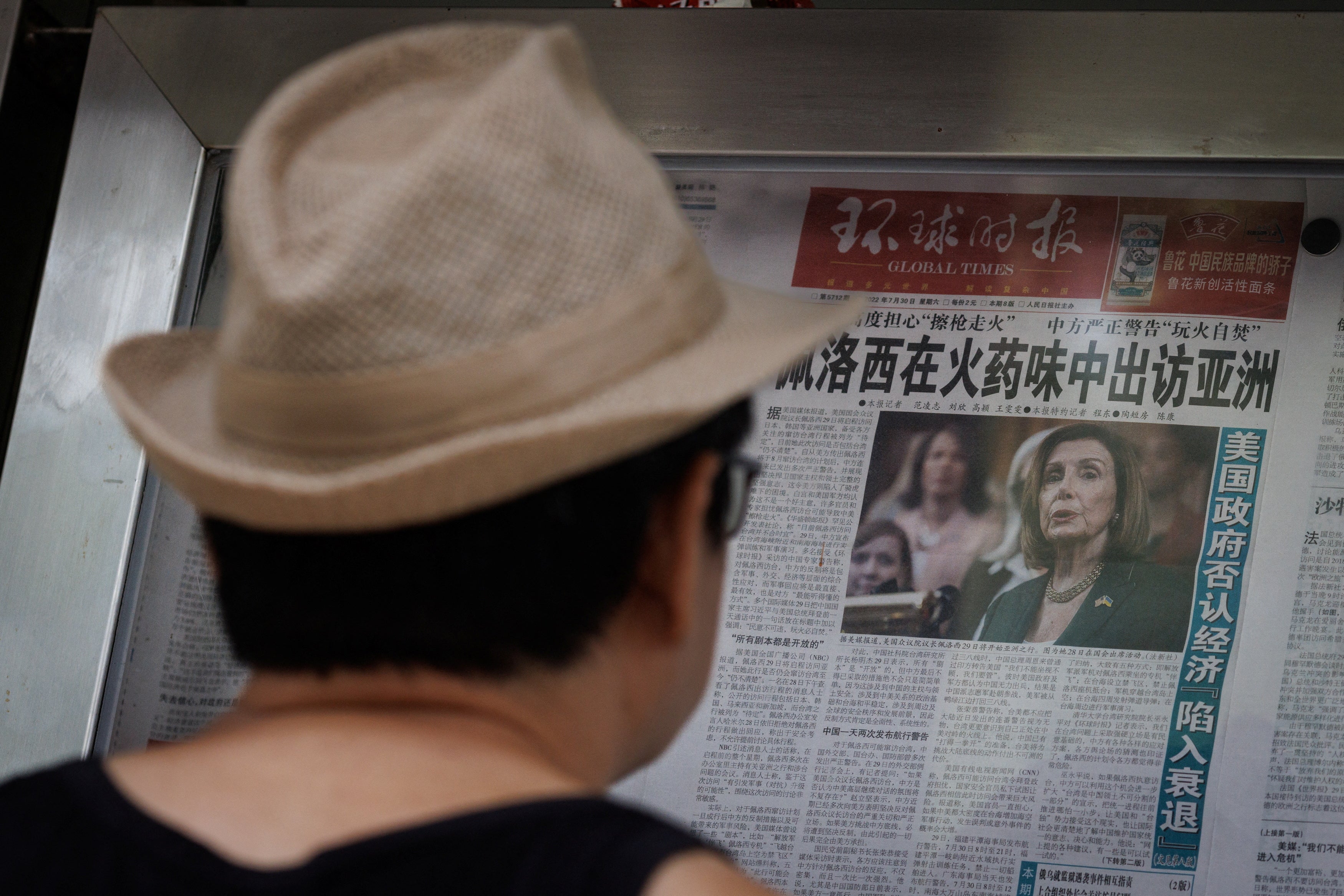 A man reads a newspaper featuring an article about Nancy Pelosi’s Asia tour on a street display wall in Beijing
