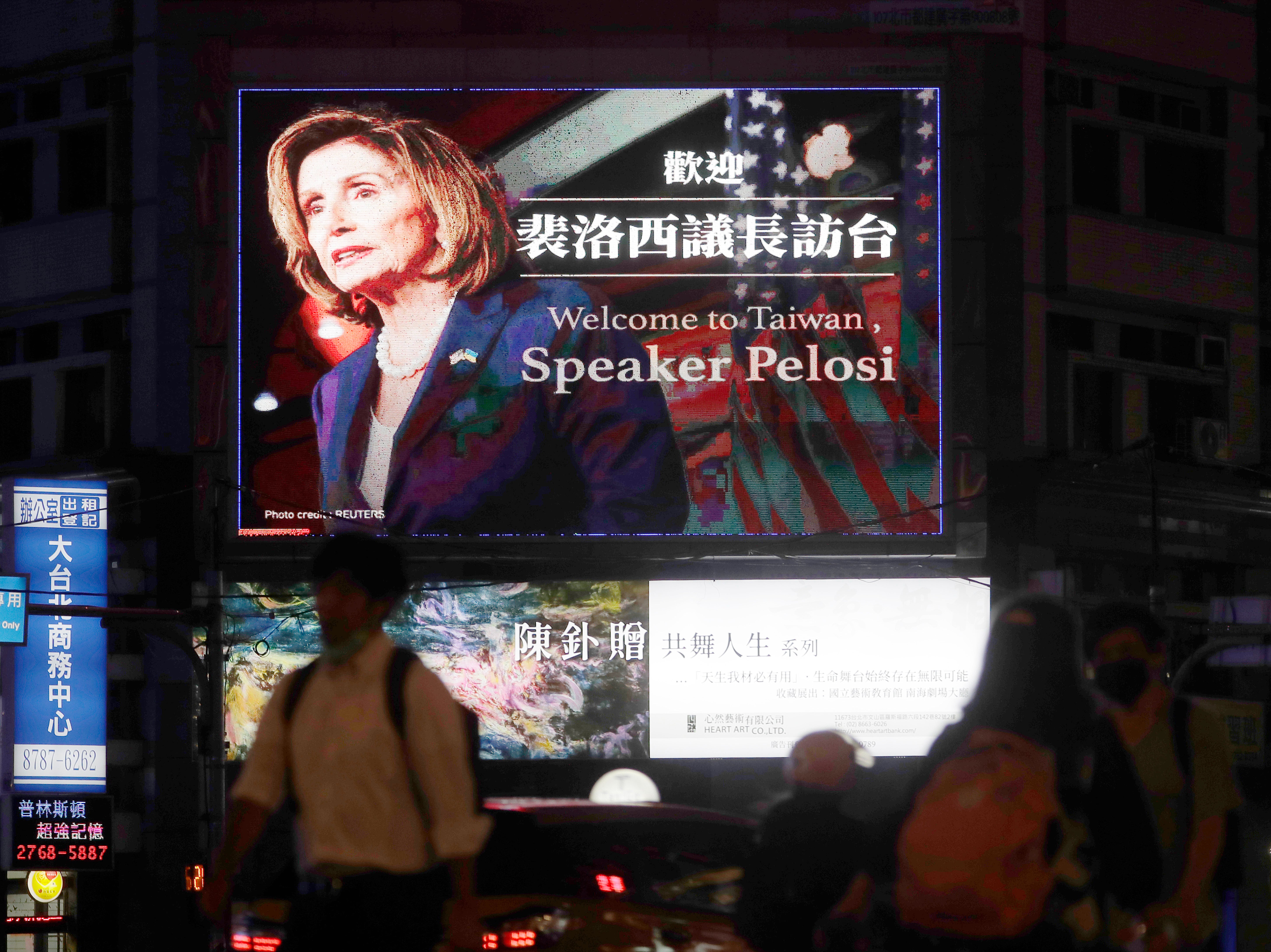 People walk past a billboard welcoming U.S. House Speaker Nancy Pelosi, in Taipei, Taiwan, Tuesday, Aug 2, 2022
