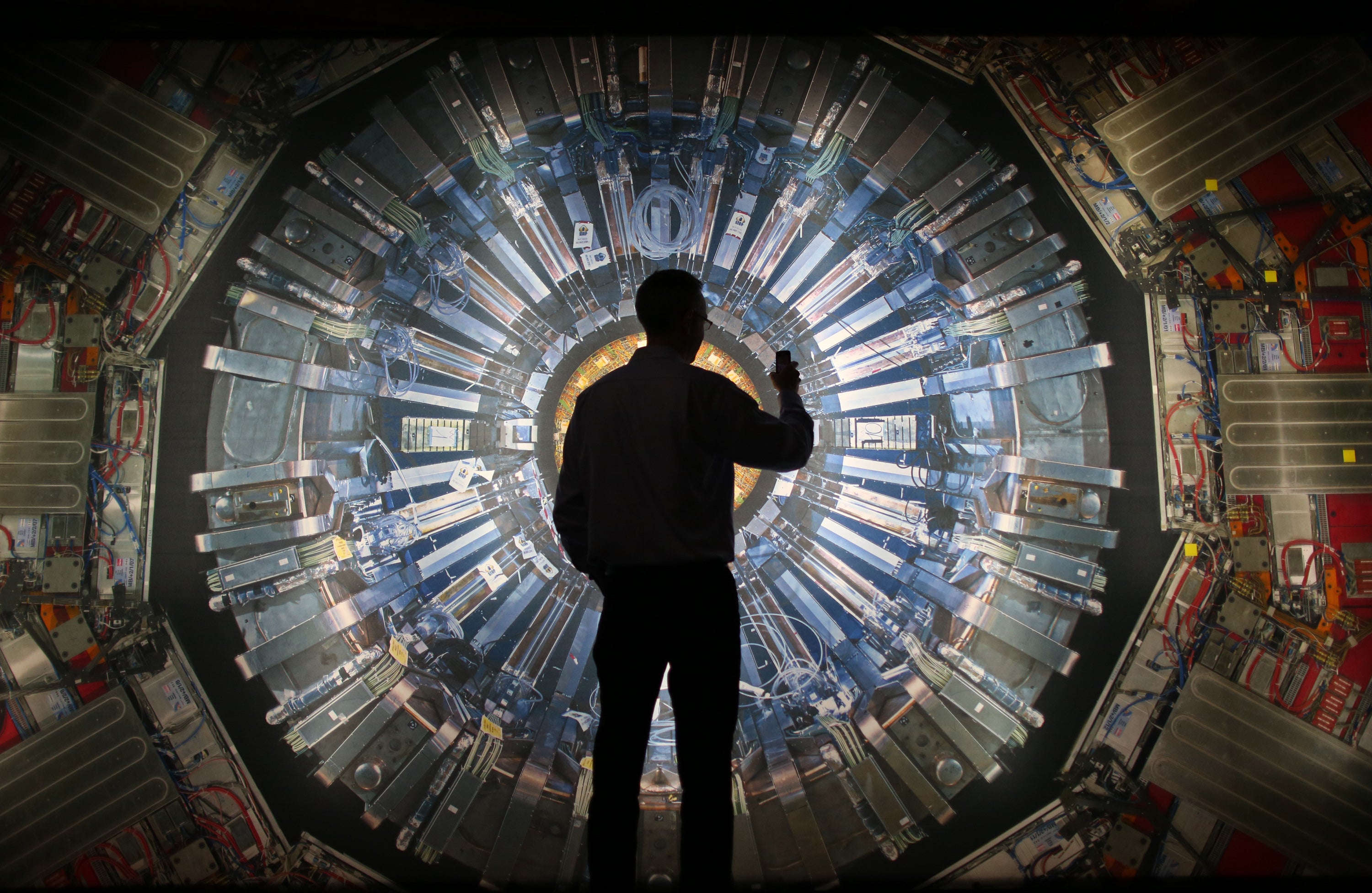 A visitor takes a photograph of a large image of the Large Hadron Collider at the London Science Museum