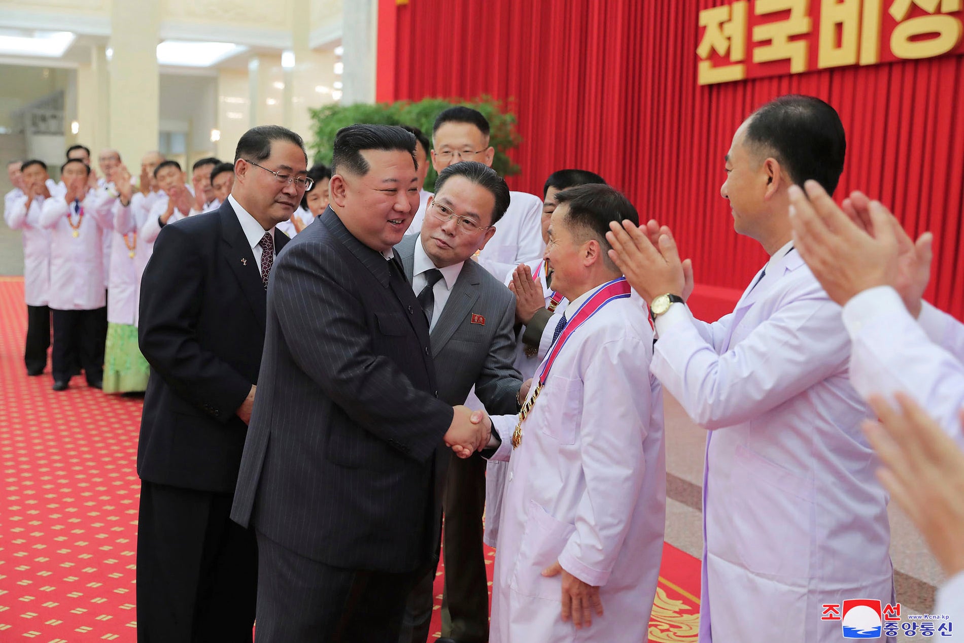 In this photo provided by the North Korean government, North Korean leader Kim Jong-un shakes hands with a health official in Pyongyang, North Korea, Wednesday, Aug. 10, 2022. Kim declared victory over Covid-19 and ordered an easing of preventive measures
