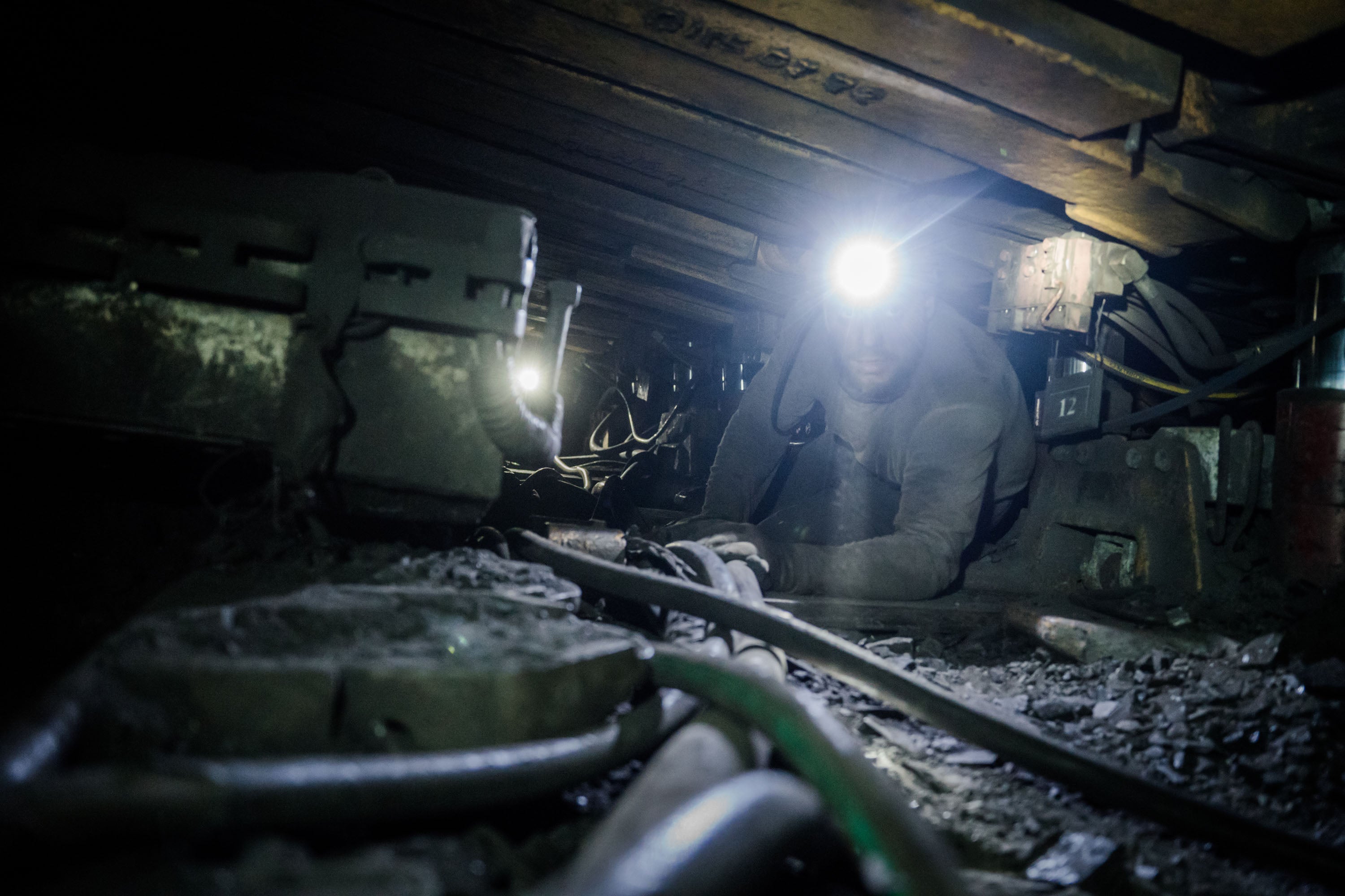 A miner operates an excavator in a cramped corridor deep underground