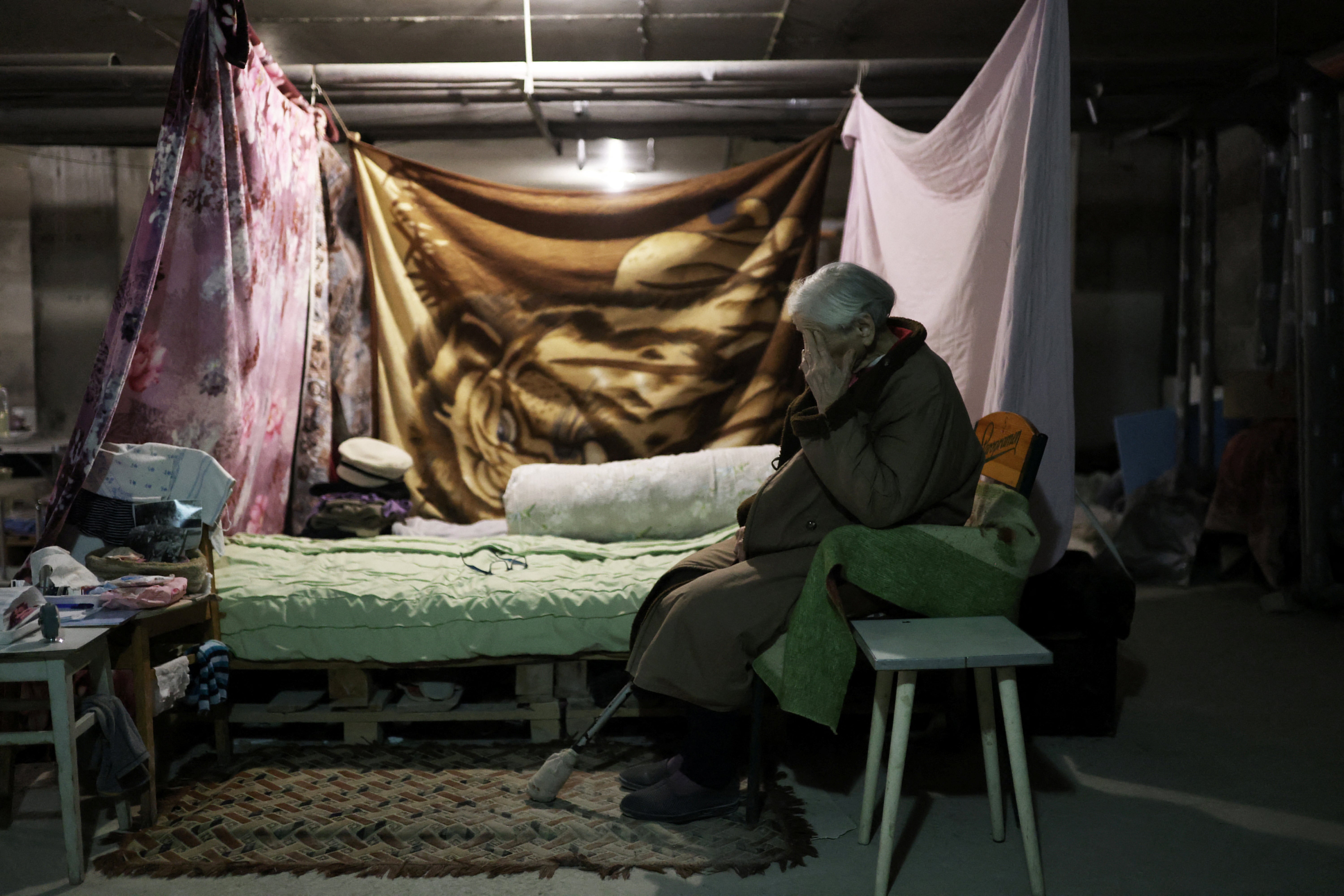 Maria gestures next to her makeshift bedroom inside a basement