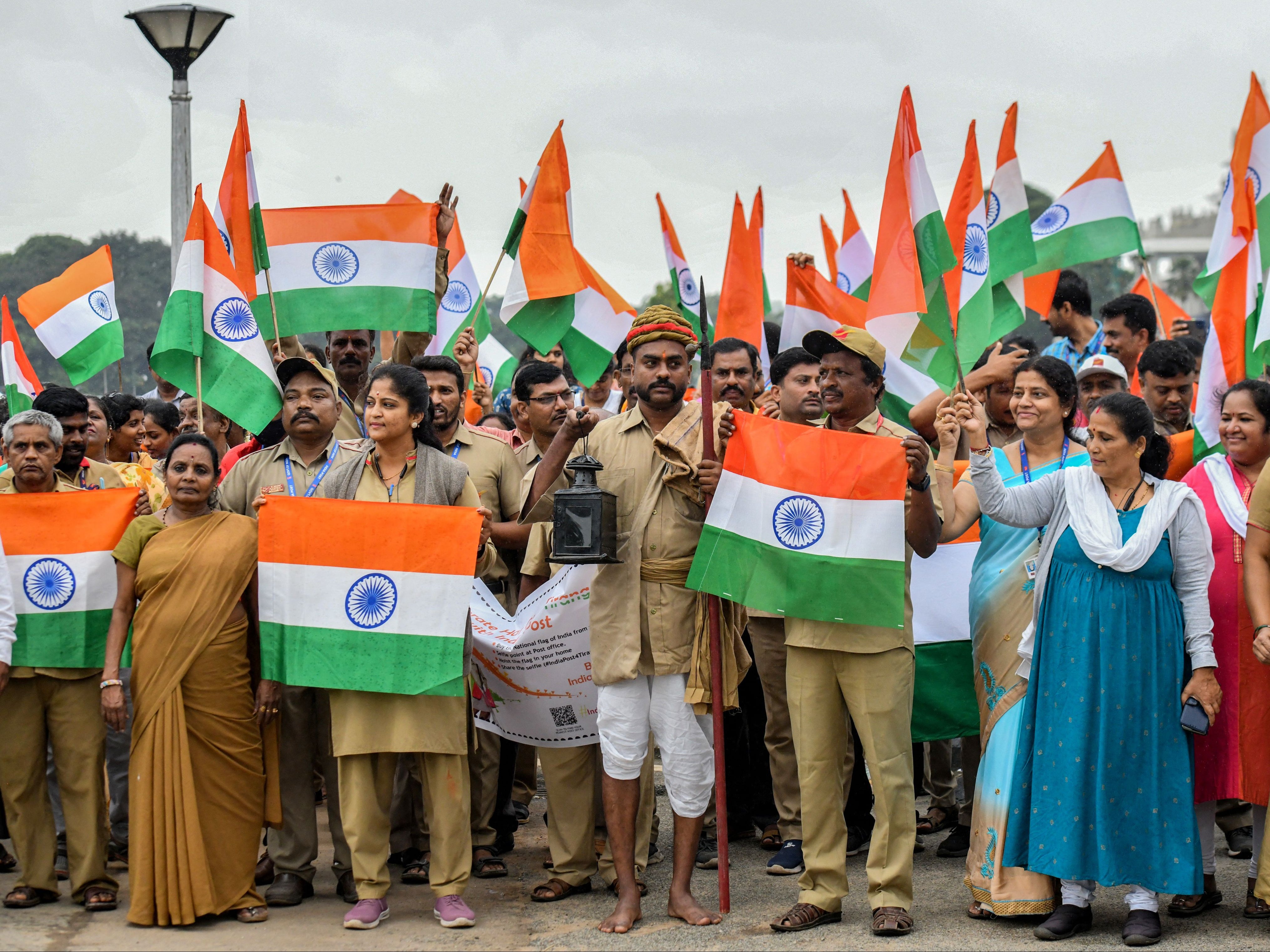 Employees of the postal department wave the Indian flag as they pass the Vidhana Soudha building during Tiranga Yatra