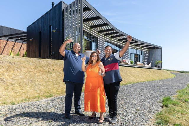 <p>Uttam Parmar, 58, with his wife Raki and son Aaron, celebrating in front of the £3,000,000 property he has won in Cornwall (Omaze/PA)</p>