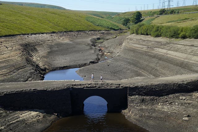 People walk across the dry cracked earth at Baitings Reservoir in Ripponden, West Yorkshire, where water levels are significantly low (Danny Lawson/PA)