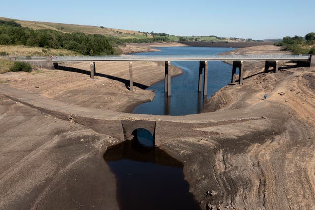 <p>A member of the public crosses an ancient packhorse bridge exposed by low water levels at Baitings Reservoir in Yorkshire</p>