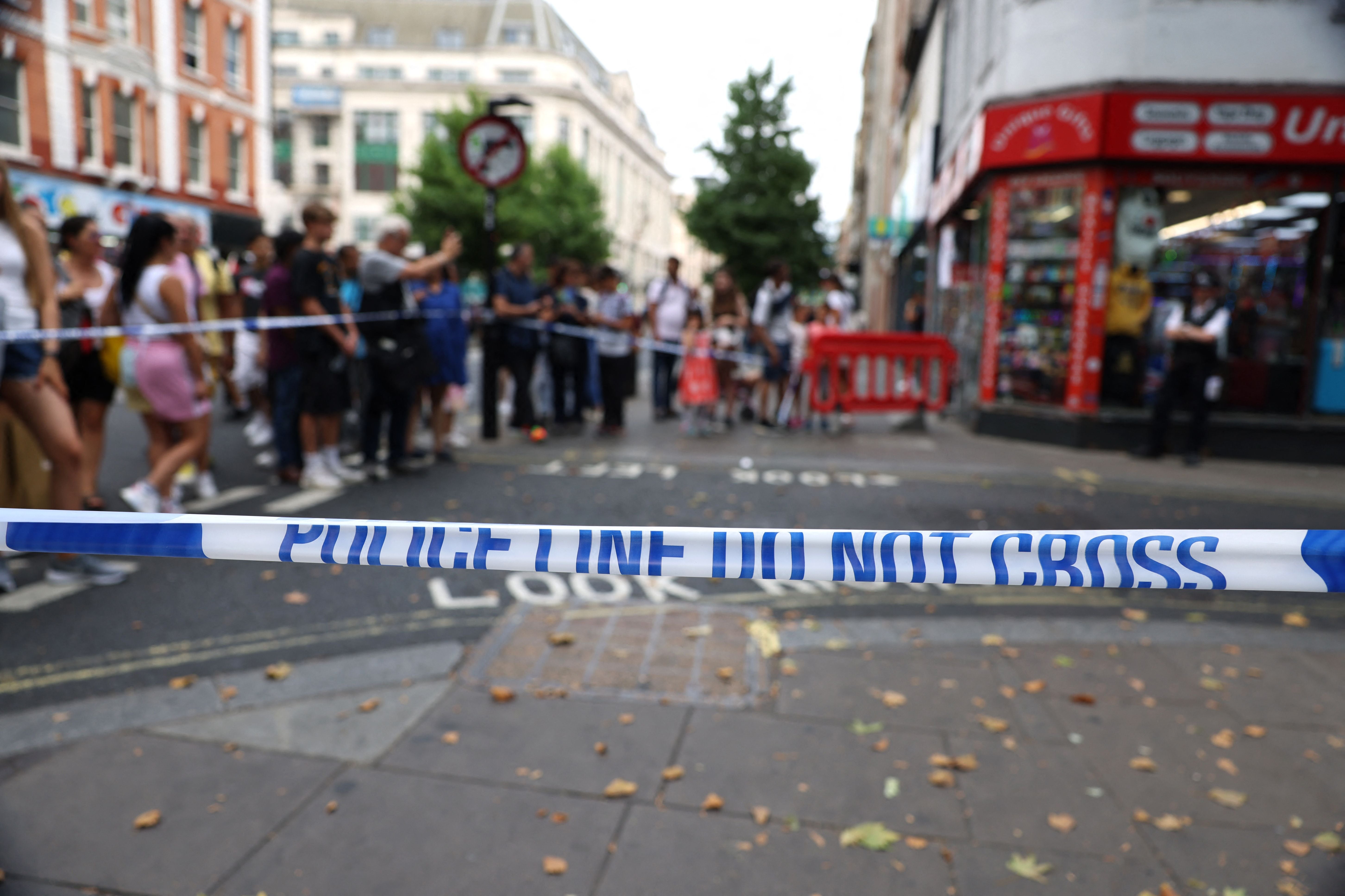 Pedestrians gather behind a police cordon near the scene of the stabbing