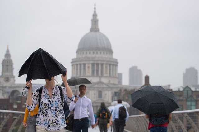 Pedestrians shelter under umbrellas as they cross the Millennium Bridge (Dominic Lipinski/PA)