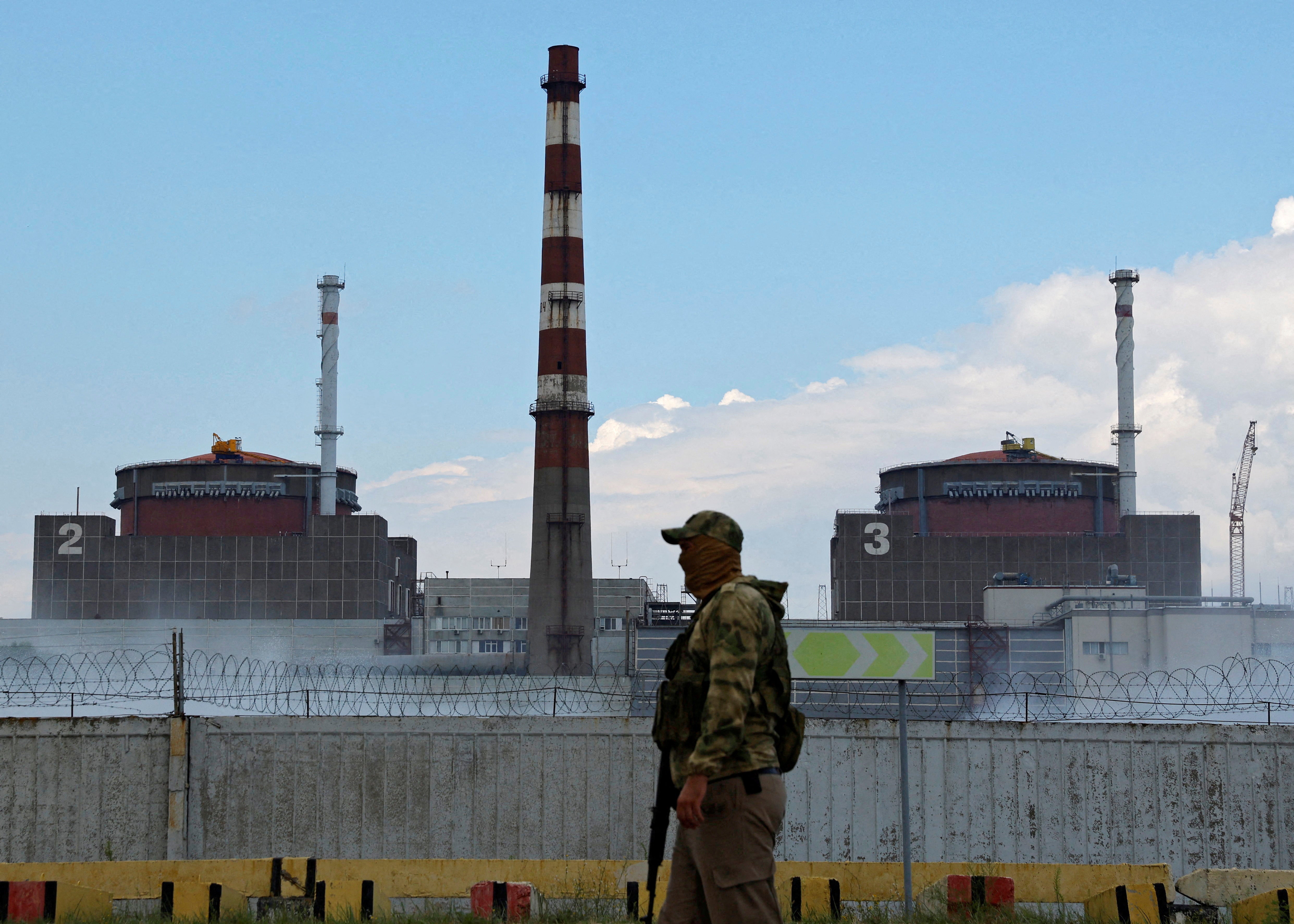 A serviceman with a Russian flag on his uniform stands guard near the Zaporizhzhia plant