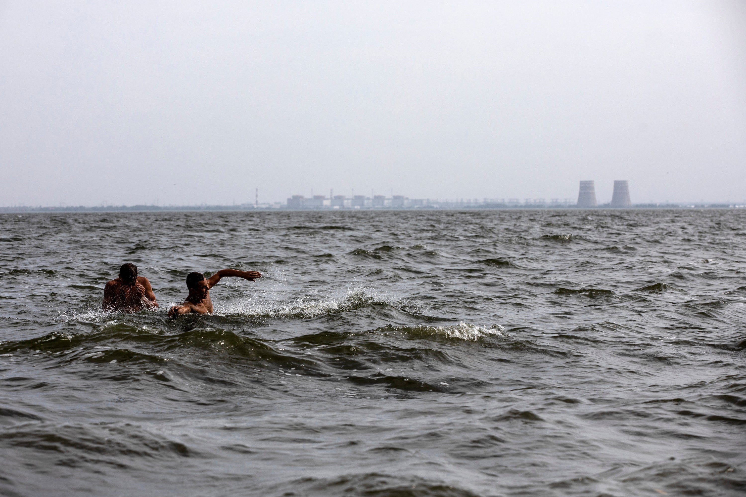 Men swim in Ukraine's Dnieper River, across from the Zaporizhzhia nuclear complex, which is under the control of Russian forces