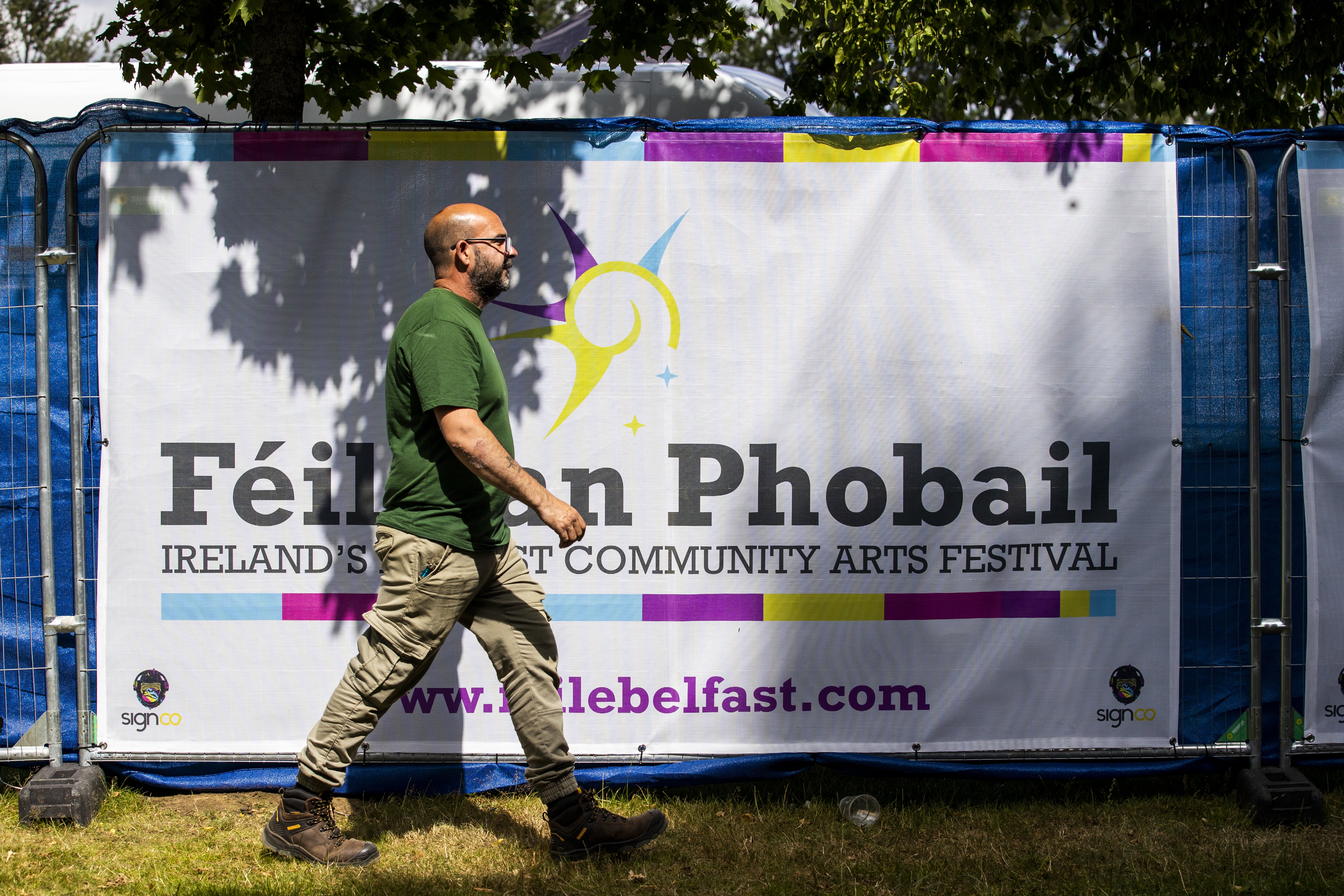 A man walks past a banner for Feile an Phobail, also known as the West Belfast Festival, in the Falls Park. (PA)