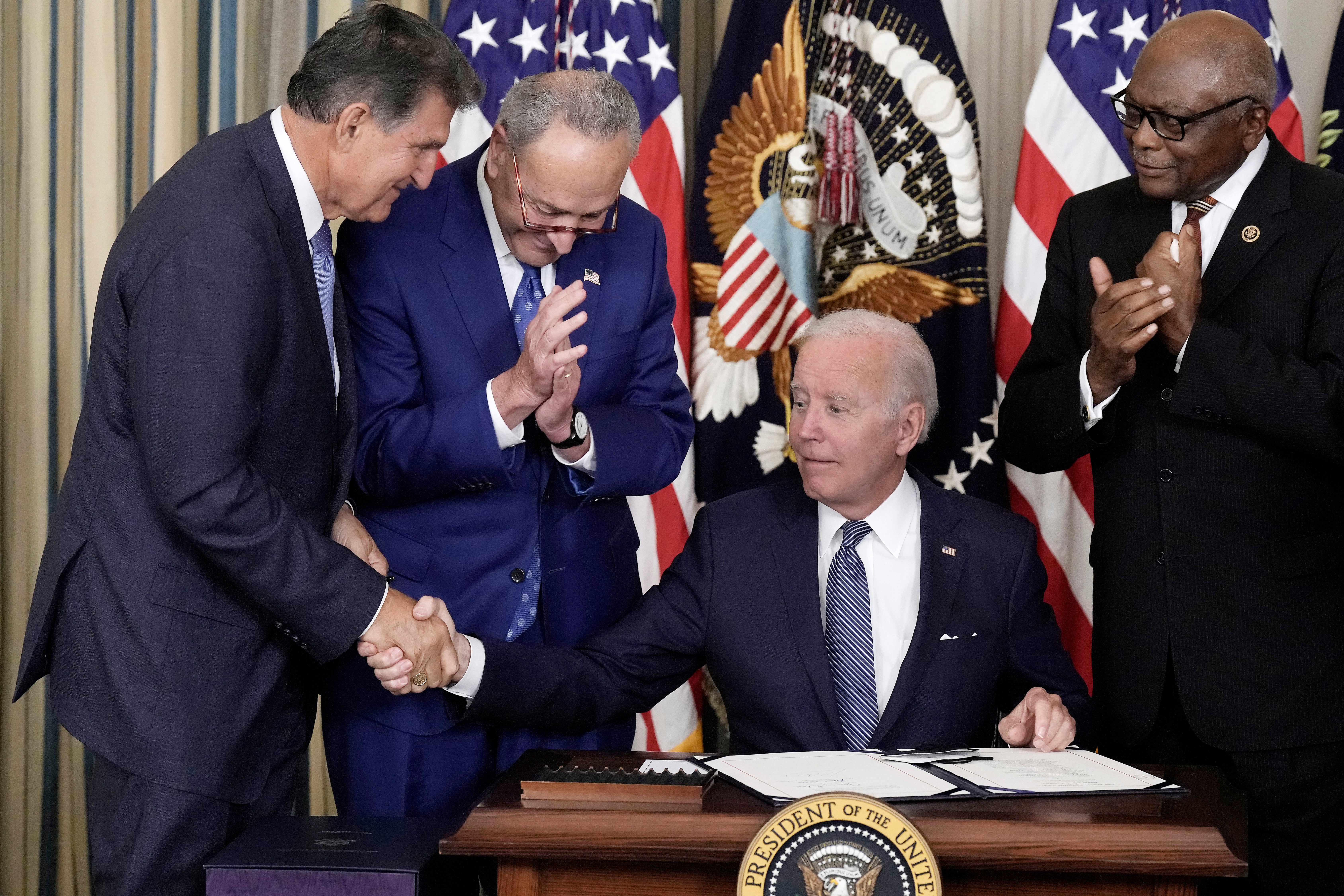 President Joe Biden shakes hands with Sen Joe Manchin (L) after signing The Inflation Reduction Act